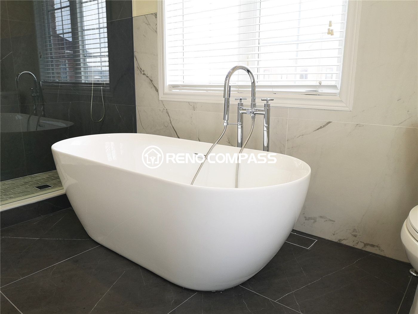 This clean and minimal bathroom renovation highlights a smooth, freestanding soaking tub set against marble wall tiles. A luxurious Richmond Hill project by Reno Compass.