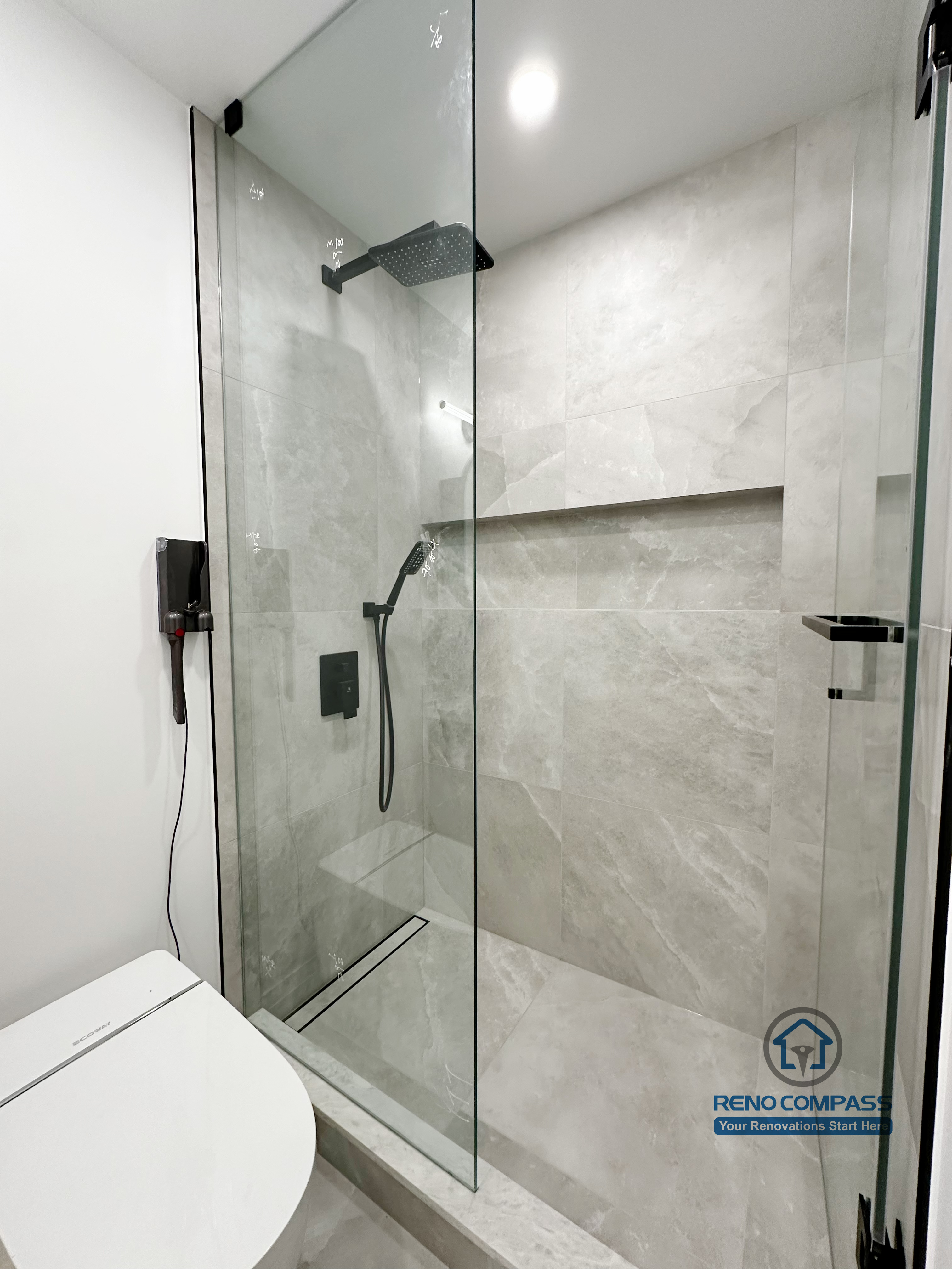Bathroom renovation in Markham featuring a compact frameless glass shower with large-format tile walls, built-in shower niche, and matte black fixtures. The layout maximizes space efficiency while maintaining a clean, modern, and easy-to-maintain design.