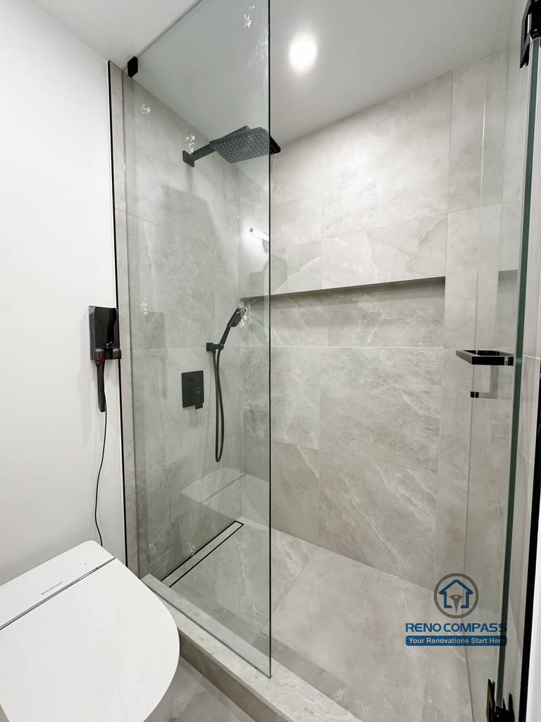 Bathroom renovation in Markham featuring a compact frameless glass shower with large-format tile walls, built-in shower niche, and matte black fixtures. The layout maximizes space efficiency while maintaining a clean, modern, and easy-to-maintain design.