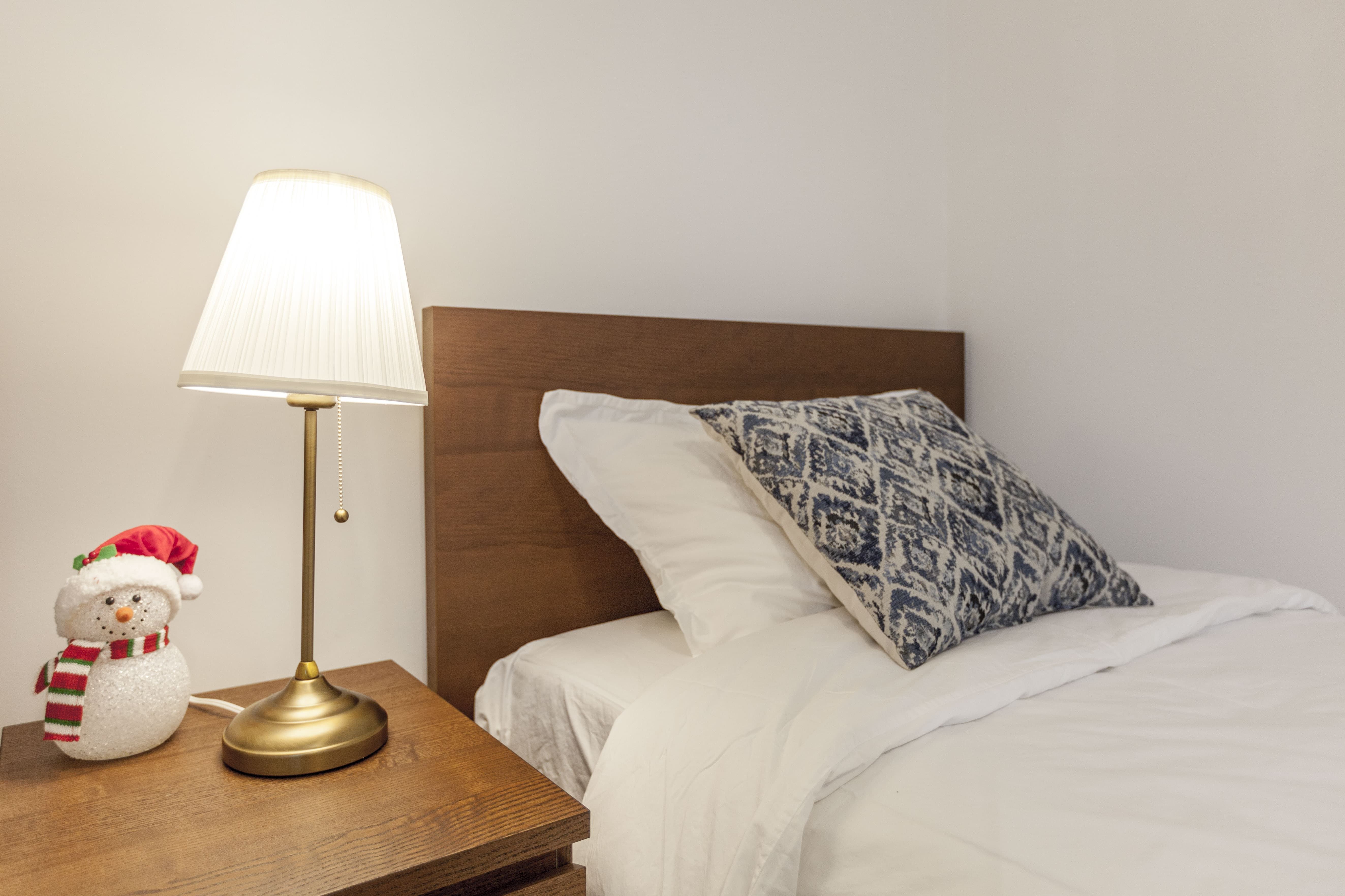 This Toronto bedroom renovation highlights a warm and cozy sleeping environment with a clean bed setup, wooden headboard, and matching nightstand. Soft lighting from the bedside lamp enhances comfort, creating a relaxing atmosphere ideal for modern living. The simple yet functional design reflects the attention to detail of a professional Toronto Renovation Company.