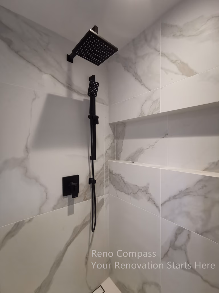 This image highlights a modern shower detail completed as part of a Markham interior renovation. Large-format marble-look wall tiles create a seamless and spacious visual effect, while built-in niche shelving provides practical storage without disrupting the clean lines. Matte black shower fixtures add strong contrast and a contemporary edge, balancing aesthetics with durability. The layout prioritizes ease of use, low maintenance, and long-term comfort, resulting in a bathroom space that feels refined, functional, and timeless.