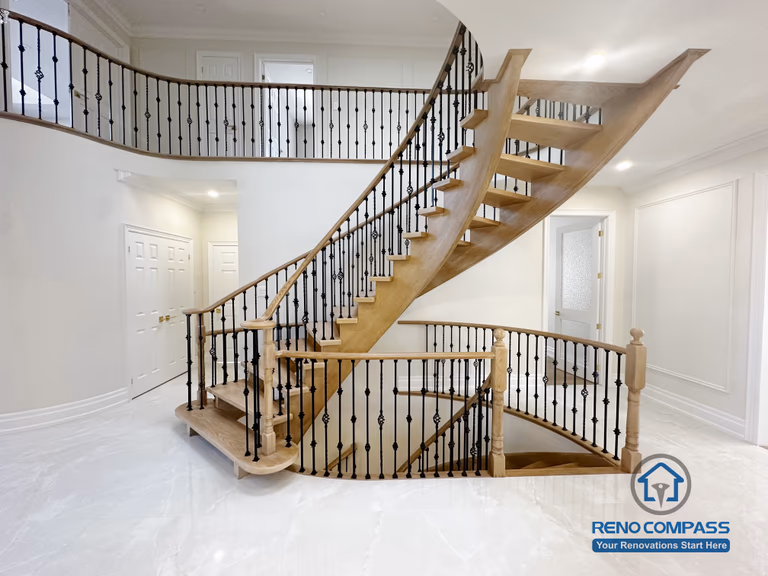 This image showcases the front view of a grand curved staircase as part of a North York flooring and stair renovation. The staircase features solid hardwood treads, smooth curved stringers, and decorative iron balusters, forming a strong architectural focal point at the home’s entrance. The surrounding flooring is finished with polished, light-toned surfaces that enhance brightness and reflect natural light. This renovation highlights precise craftsmanship and seamless coordination between flooring and stair design, creating an elegant and cohesive interior for North York homes.