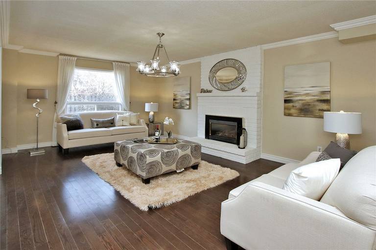 This Toronto interior design pre-sale staging features a spacious luxury living room with rich hardwood flooring, modern chandelier, and a stylish fireplace feature wall. Neutral-tone sofas, elegant décor, and soft natural lighting create a warm and sophisticated atmosphere that highlights comfort and space.