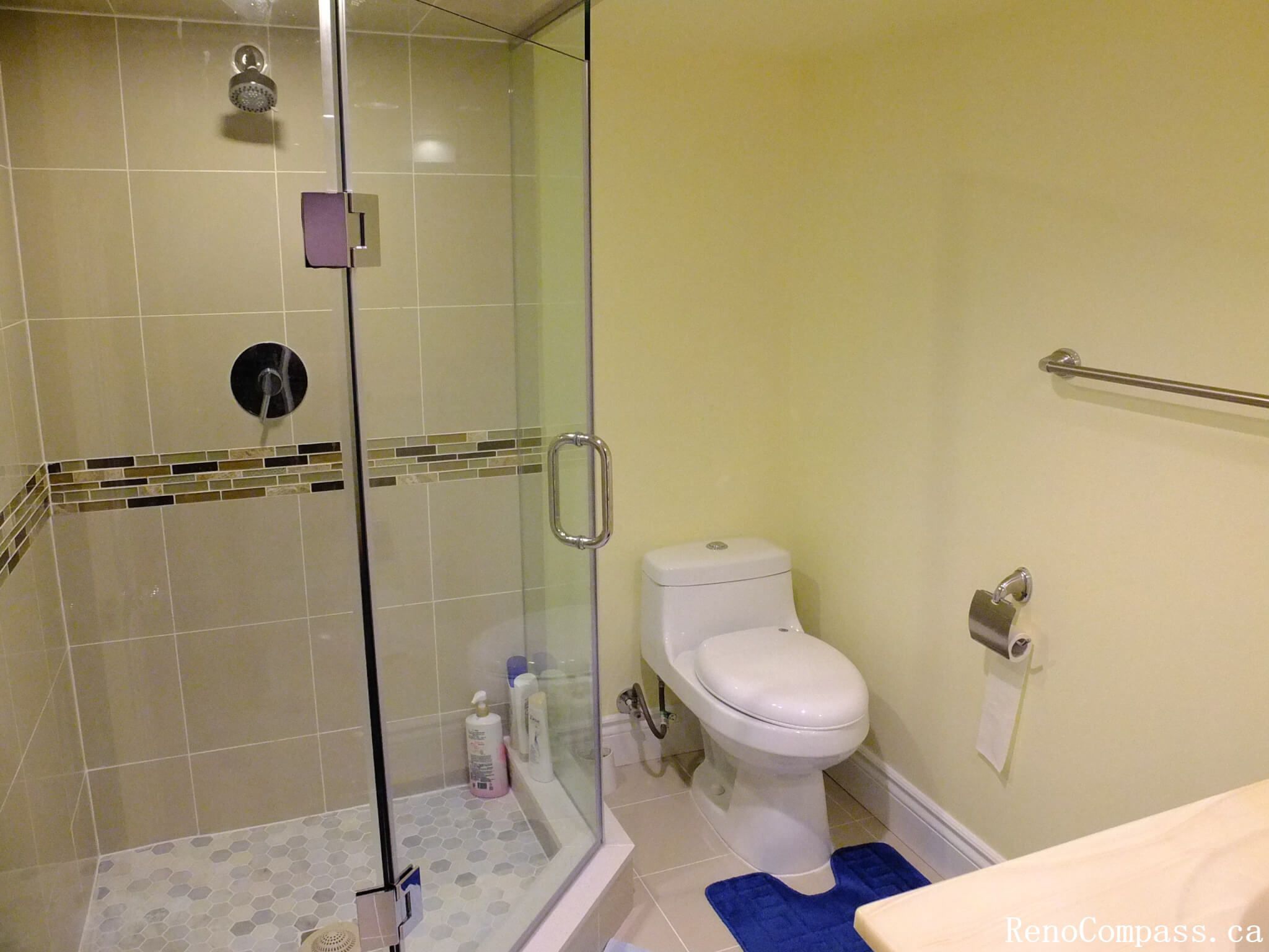 This bathroom renovation project in Mississauga features a modern glass shower enclosure with clean tile finishes and a mosaic accent strip. The walk-in shower is designed with a frameless glass door, neutral wall tiles, and a pebble-style shower floor that enhances both comfort and safety. Paired with upgraded fixtures, toilet installation, and functional layout improvements, this renovation creates a bright and practical bathroom space suitable for everyday living. The design balances simplicity, durability, and modern aesthetics to elevate the overall interior environment.