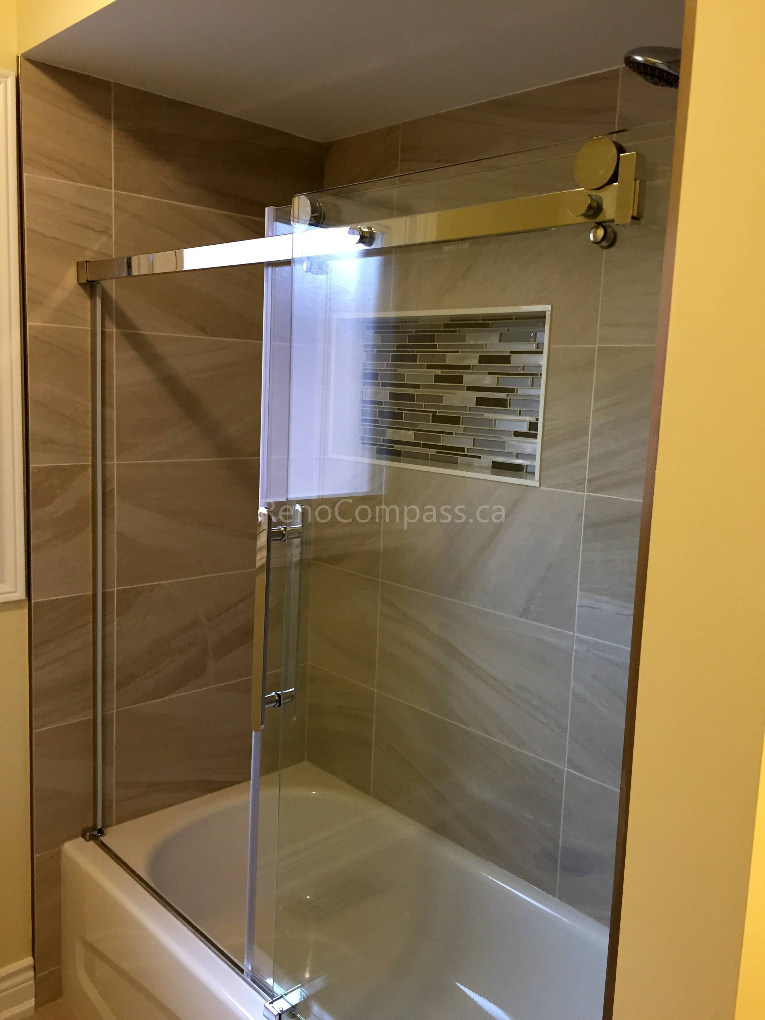 This Toronto bathroom renovation by Reno Compass features a modern bathtub-shower combination with a sleek sliding glass shower door and contemporary wall tiles. The neutral-toned tiles create a warm and elegant atmosphere, while the built-in niche adds convenient storage for daily essentials. High-quality fixtures and precise installation enhance durability, functionality, and visual appeal, delivering a clean and modern bathroom upgrade for everyday comfort.