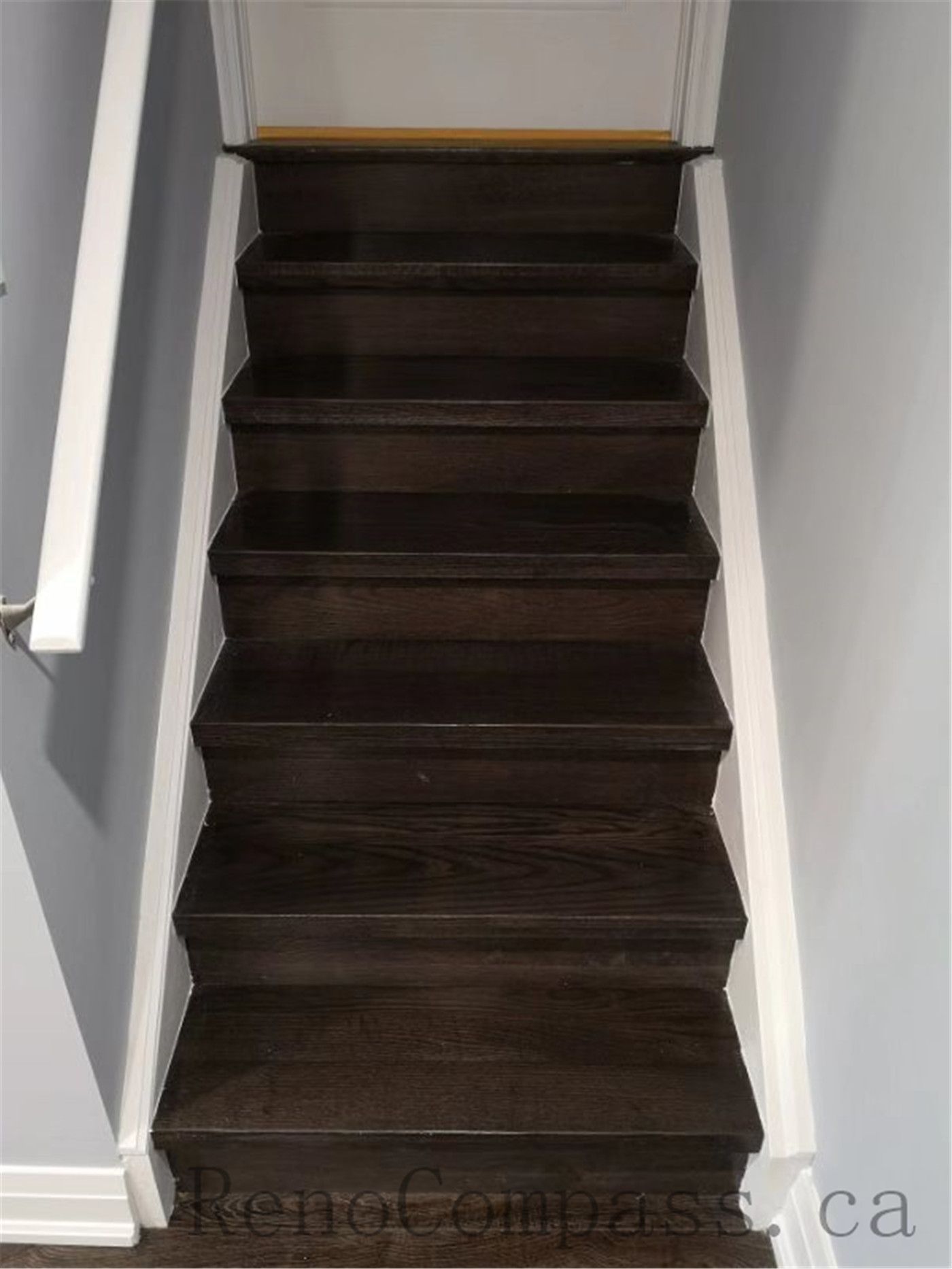 This stylish basement staircase renovation in Aurora highlights dark wood steps with crisp white trim and smooth wall finishes. A seamless connection between levels, designed by Reno Compass.