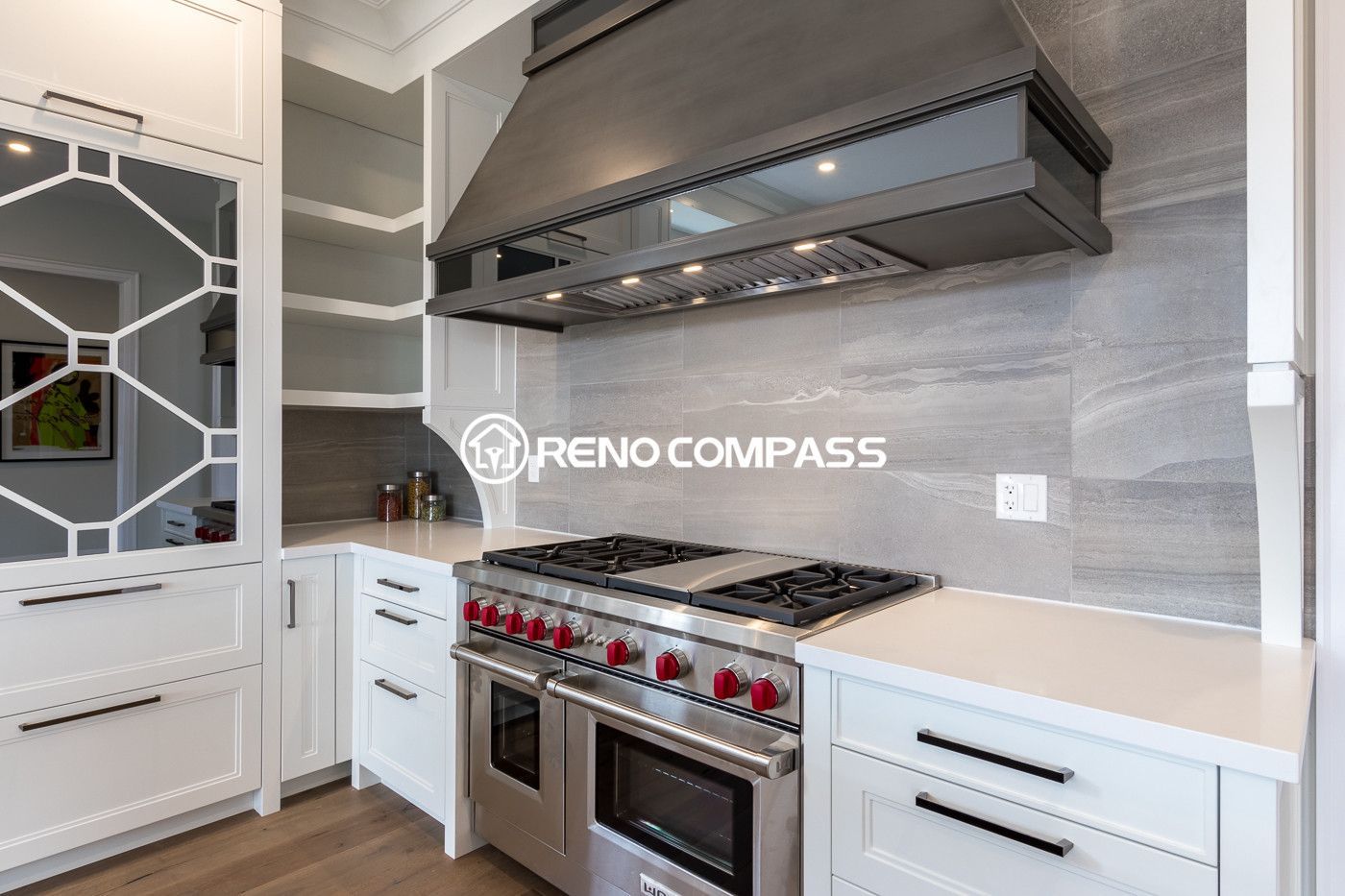 High-end kitchen renovation in Newmarket featuring a custom-built range hood, professional gas stove, and modern white cabinetry with stone backsplash. This elegant kitchen design combines functionality and style, creating a luxurious cooking space within a beautifully renovated open-concept home.