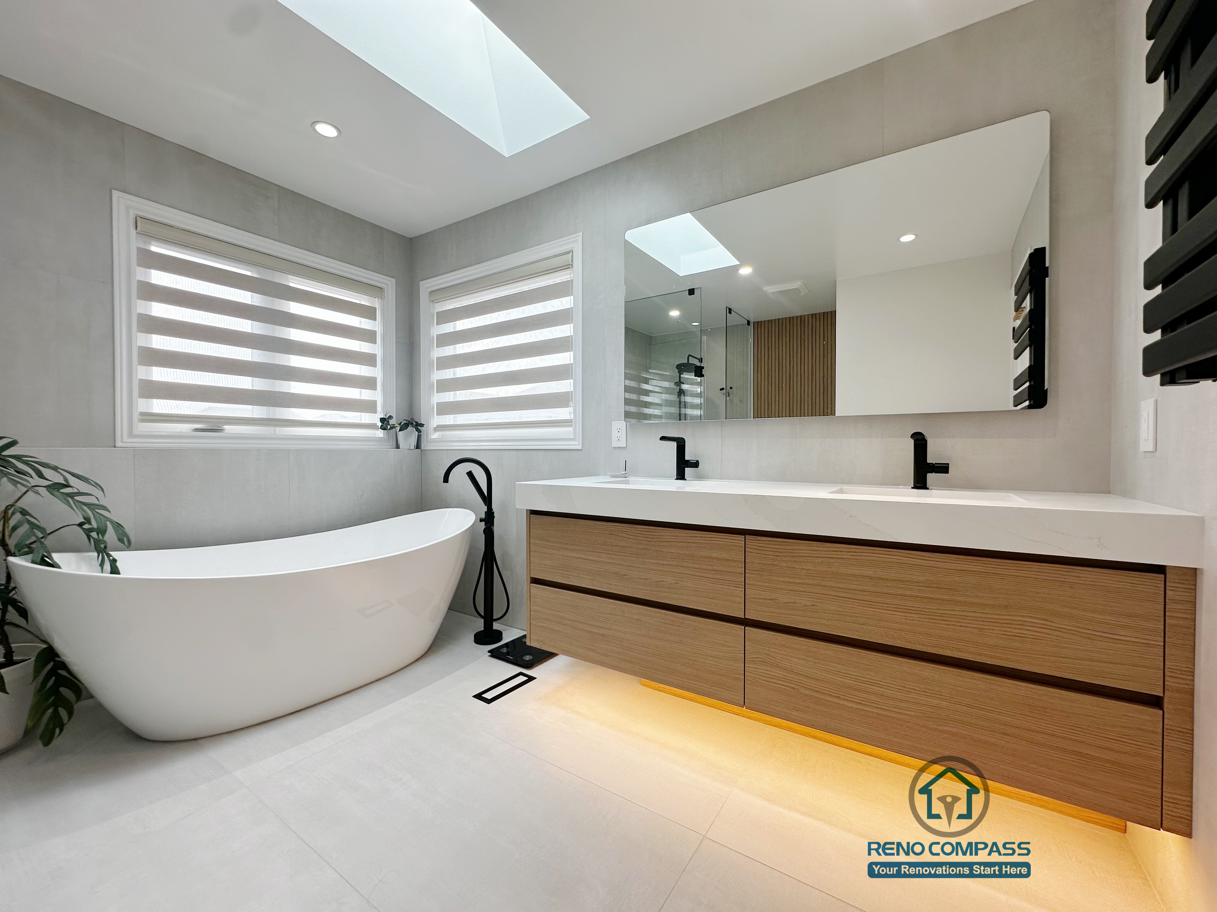 A modern curbless bathroom renovation completed by Reno Compass in Markham, Toronto.
This design features a freestanding bathtub placed by natural light, a floating double-sink vanity with warm wood tones, and soft under-cabinet lighting that enhances both functionality and atmosphere.