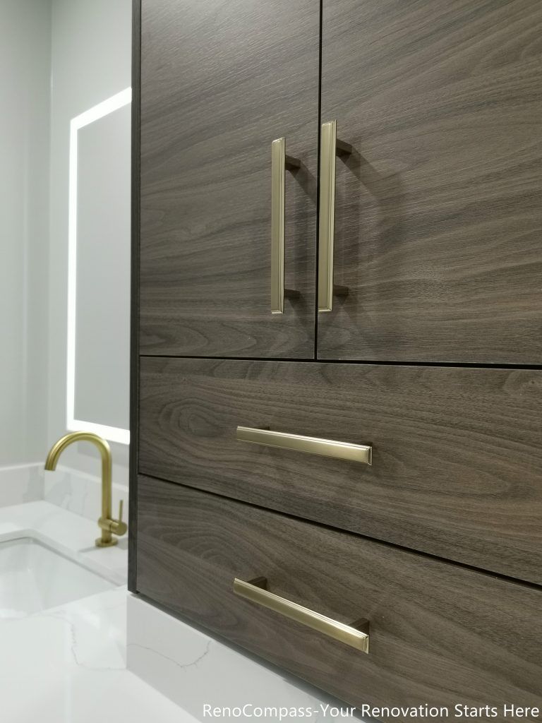 This Oakville master bathroom renovation showcases a custom-built modern vanity cabinet featuring rich wood grain finishes, quartz countertop, and elegant brushed gold hardware. The integrated storage design maximizes functionality while maintaining a clean, contemporary aesthetic. Paired with a stylish undermount sink and illuminated mirror, this upgrade enhances both daily convenience and visual appeal. Completed by a trusted Toronto renovation company, this bathroom vanity installation delivers a perfect balance of luxury, durability, and practical storage solutions.