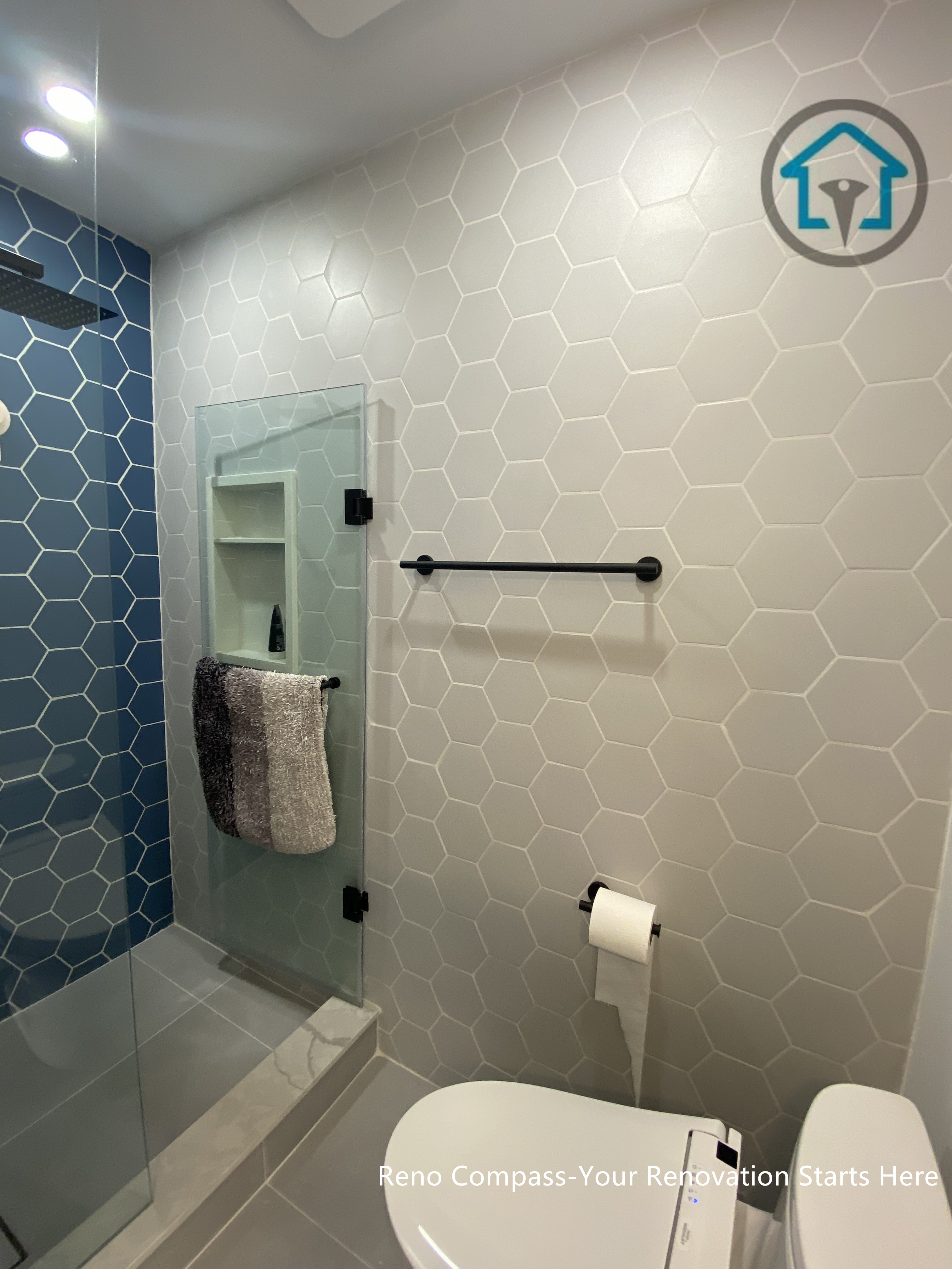 This bathroom renovation in Toronto showcases a clean, modern shower design featuring hexagon tile walls and a frameless glass enclosure. The contrast between light neutral tiles and the deep blue accent wall adds visual depth while maintaining a calm, contemporary aesthetic. Integrated shower niches, matte black fixtures, and a linear layout improve everyday functionality without overwhelming the space. Careful tile alignment and minimal detailing create a refined finish that balances durability, ease of maintenance, and long-term usability.