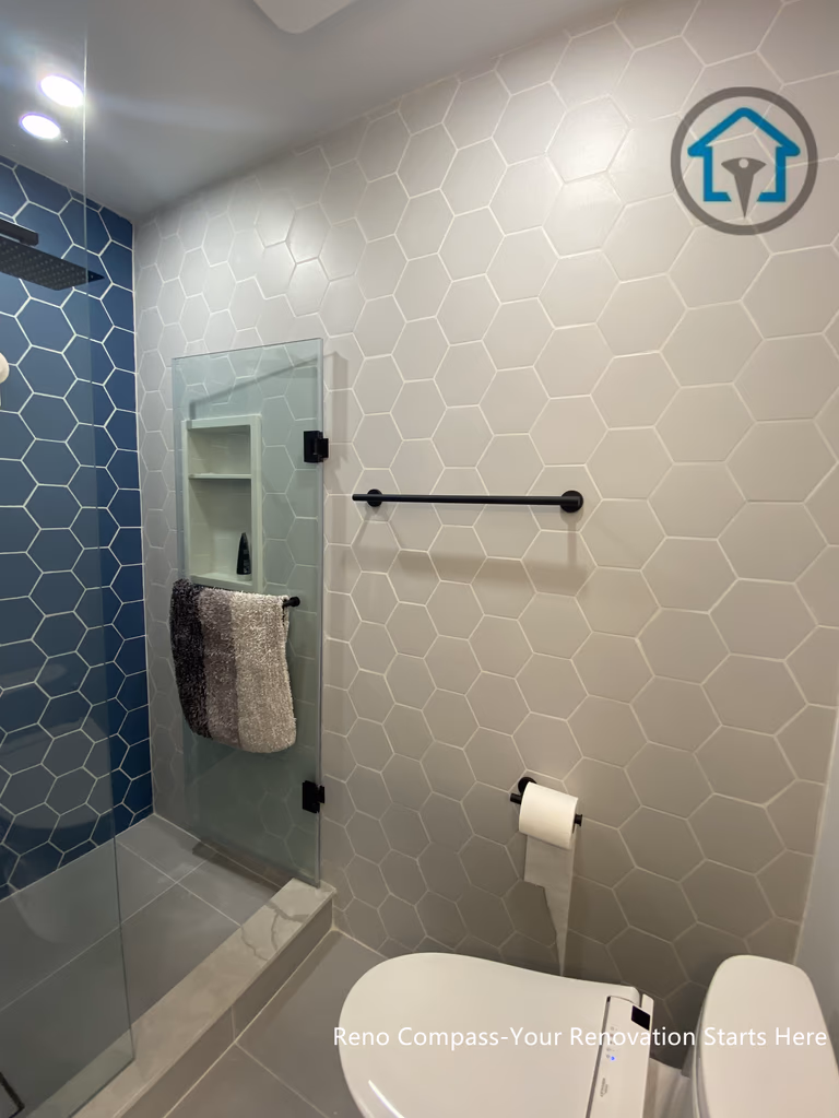 This bathroom renovation in Toronto showcases a clean, modern shower design featuring hexagon tile walls and a frameless glass enclosure. The contrast between light neutral tiles and the deep blue accent wall adds visual depth while maintaining a calm, contemporary aesthetic. Integrated shower niches, matte black fixtures, and a linear layout improve everyday functionality without overwhelming the space. Careful tile alignment and minimal detailing create a refined finish that balances durability, ease of maintenance, and long-term usability.