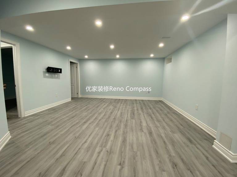 This Aurora basement renovation showcases a spacious open-concept living area completed by a professional Toronto renovation company. The upgraded basement features modern vinyl plank flooring, smooth finished ceilings with LED pot lights, and clean neutral wall tones that enhance brightness and comfort. The open layout seamlessly connects the living space to the laundry and bedroom areas, creating a functional and versatile basement ideal for family entertainment, rental use, or extended living. Contractor: Reno Compass Inc.