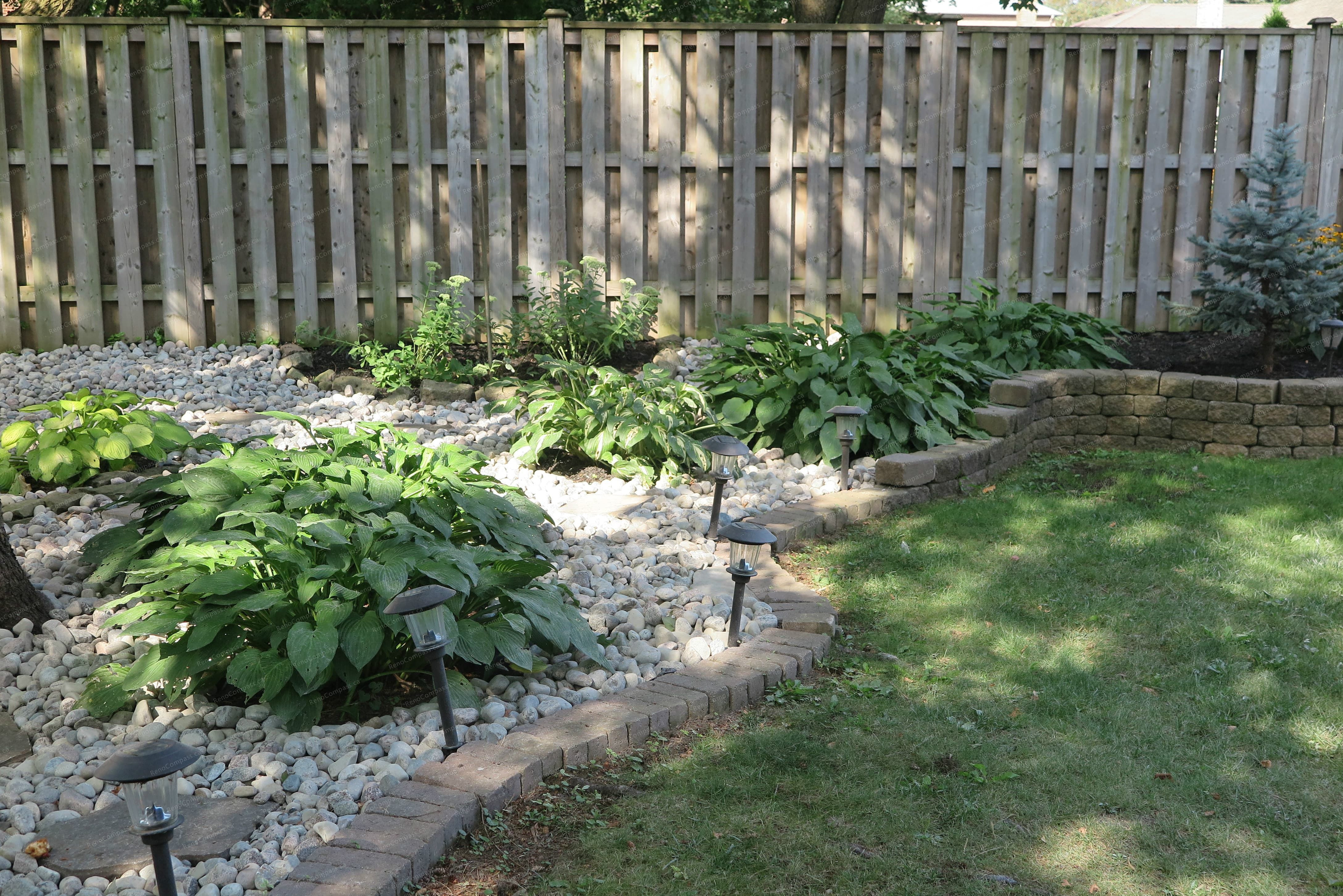 This image showcases a finished North York landscaping renovation featuring a low-maintenance decorative stone garden with natural stepping stones, mature trees, and integrated pathway lighting. The design enhances backyard drainage, visual depth, and usability while creating a calm, modern outdoor environment. Completed by a Toronto Renovation Company experienced in residential landscaping and outdoor space upgrades.