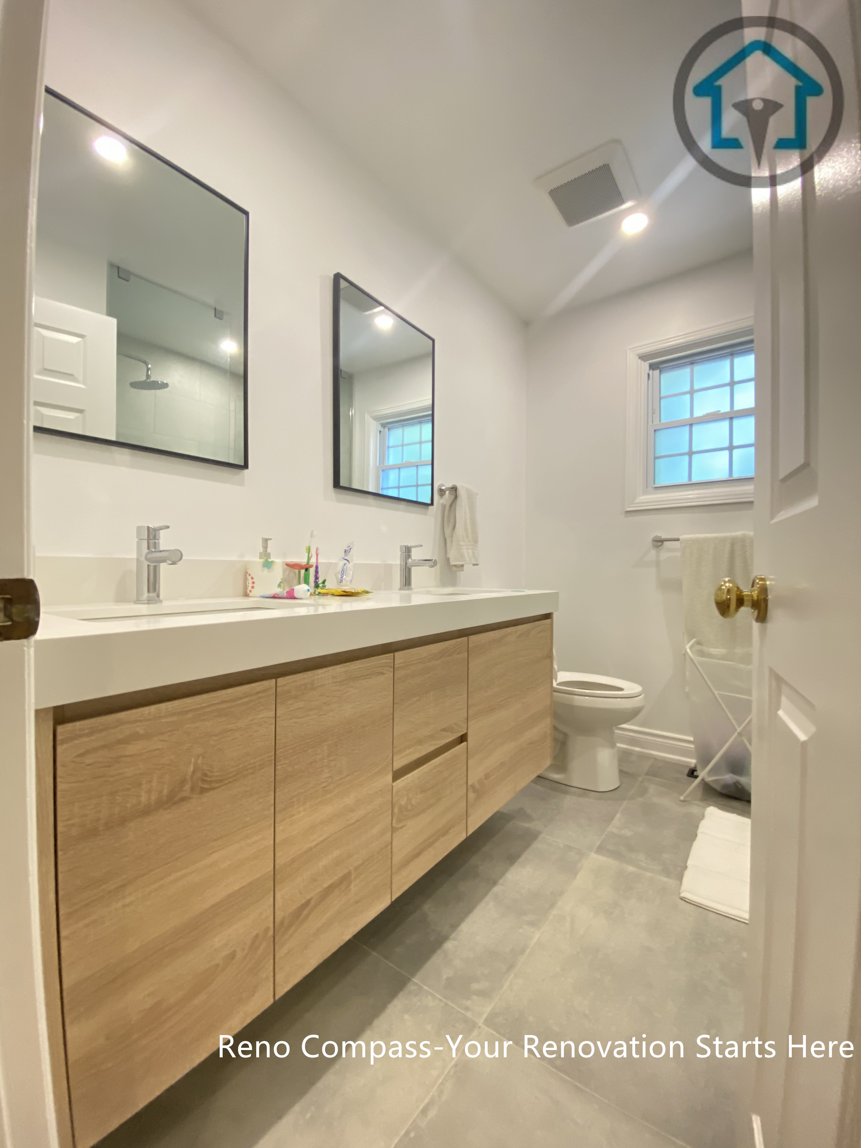 This Oakville bathroom renovation features a clean and functional layout with a custom double vanity in a natural wood finish. The floating-style cabinetry enhances visual openness while providing generous storage. Neutral floor tiles and simple wall-mounted mirrors keep the space bright and balanced, creating a practical and timeless bathroom designed for everyday use.