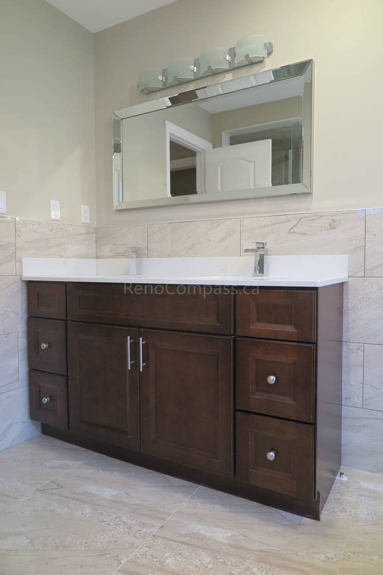 This Markham bathroom renovation features a custom dark wood vanity with a sleek quartz countertop and integrated sink, creating a clean and functional layout. Marble-style wall and floor tiles enhance the elegant and modern design, while updated lighting and mirror installation complete the refined look. Completed by Reno Compass, a professional renovation contractor specializing in bathroom renovations, vanity installation, and full interior remodeling across Markham and the Greater Toronto Area.