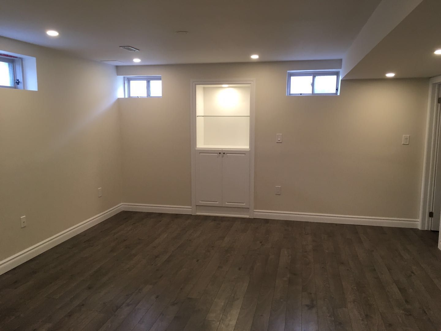 This Toronto basement renovation presents a spacious finished living area with warm wood-look flooring, recessed pot lights, and small above-grade windows that bring in natural light. A custom built-in wall niche with storage adds both functionality and visual interest. The open layout creates a flexible space ideal for a family room, entertainment area, or home office.