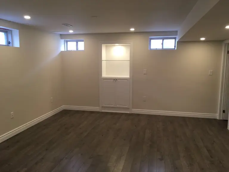 This Toronto basement renovation presents a spacious finished living area with warm wood-look flooring, recessed pot lights, and small above-grade windows that bring in natural light. A custom built-in wall niche with storage adds both functionality and visual interest. The open layout creates a flexible space ideal for a family room, entertainment area, or home office.