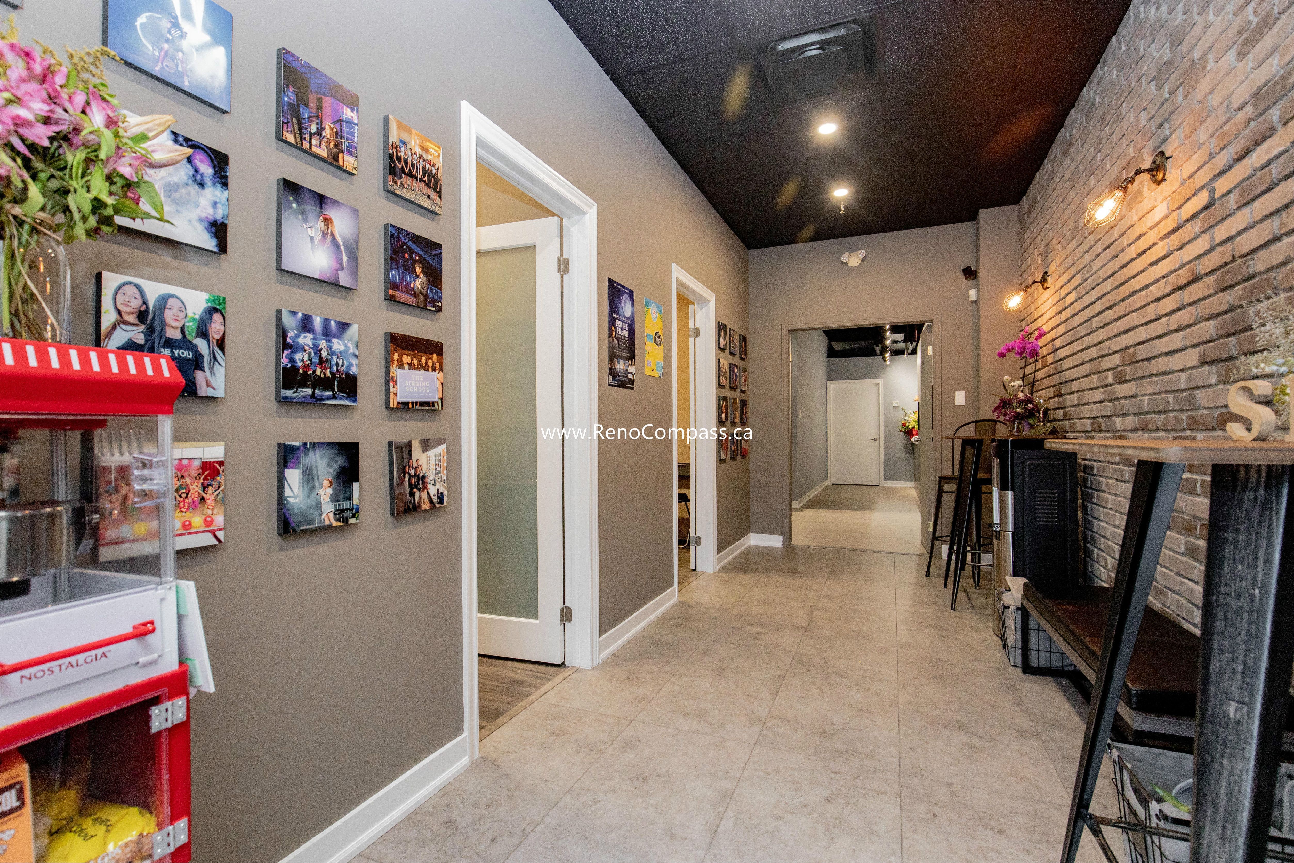 A complete commercial interior renovation in Richmond Hill featuring professional paint finishes, modern glass-panel doors, and a decorative brick feature wall. This project for The Singing School highlights a high-contrast design with a black ceiling and recessed lighting for a modern studio atmosphere.
