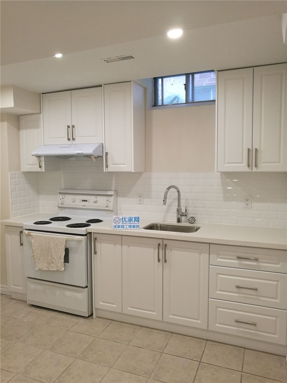 This image showcases a completed basement kitchen renovation in Markham, featuring clean white cabinetry, modern hardware, and a functional layout designed for basement living. The space includes a full set of upper and lower cabinets, durable countertops, and a practical cooking area with range hood and sink installation. Light subway-style backsplash tiles and neutral flooring create a bright and welcoming atmosphere, while the window above enhances ventilation and natural light. Completed by a professional Toronto Renovation Company, this basement kitchen upgrade focuses on efficient space planning, long-lasting materials, and modern finishes ideal for rental units, in-law suites, or extended family use.