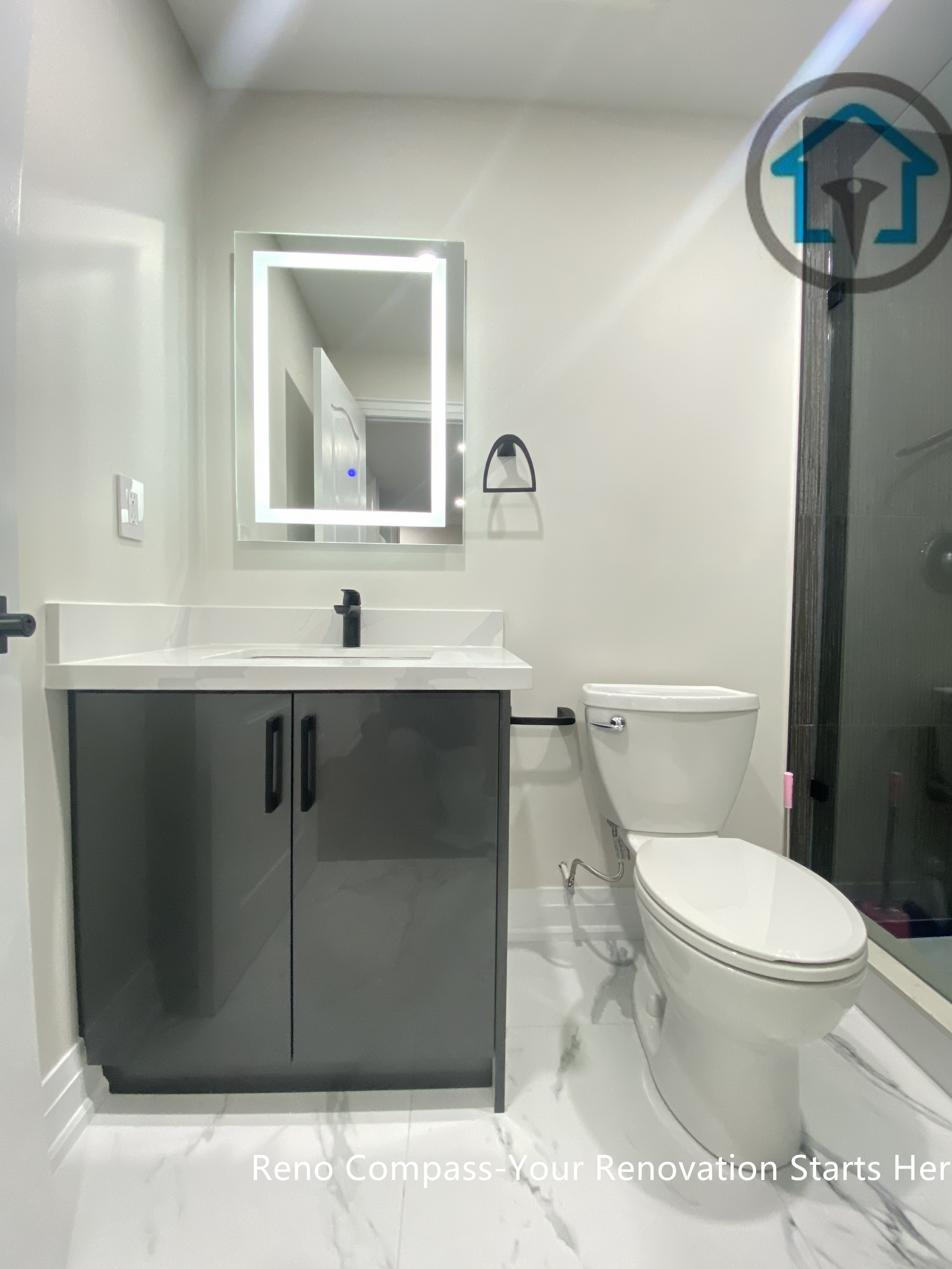 This Stouffville basement bathroom renovation highlights a frameless glass shower, large-format wall tiles, marble-look flooring, LED mirror, and modern vanity with matte black fixtures. The layout maximizes space efficiency while maintaining a clean, contemporary aesthetic, completed by Reno Compass Inc.