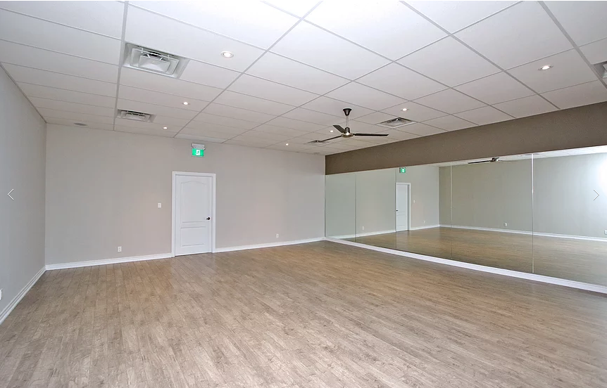 Spacious yoga practice room completed as part of a Richmond Hill commercial studio renovation. The interior upgrade features durable wood-look flooring, full mirrored wall installation, modern ceiling lighting, ventilation improvements, and a clean open layout designed for yoga and fitness classes. This renovation enhances functionality, comfort, and visual openness for group sessions, delivered by a professional Toronto renovation company specializing in commercial wellness and studio spaces.