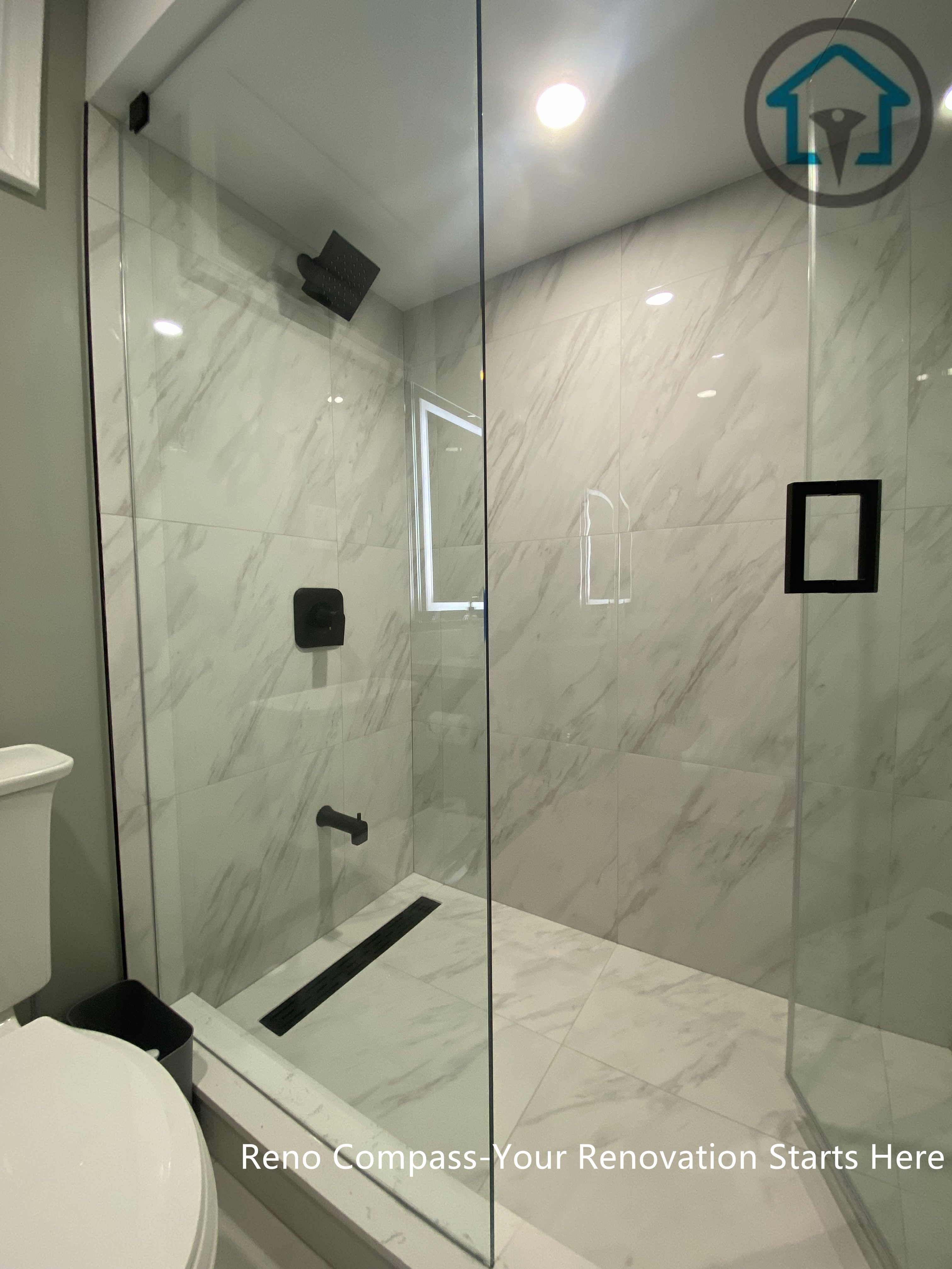 Modern walk-in shower completed as part of a Vaughan basement renovation, featuring large-format marble-style tiles, frameless glass enclosure, linear drain, and matte black fixtures. Designed for durability, easy maintenance, and a clean contemporary look by Reno Compass.