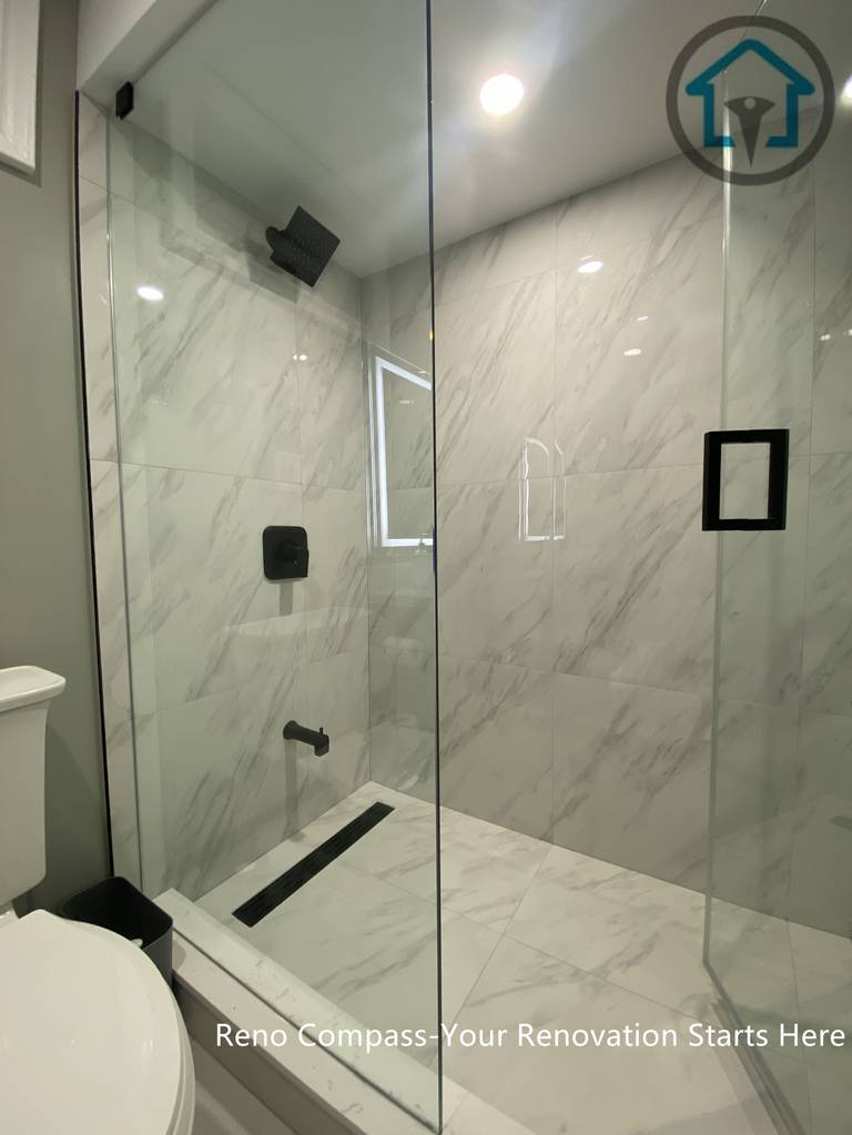 Modern walk-in shower completed as part of a Vaughan basement renovation, featuring large-format marble-style tiles, frameless glass enclosure, linear drain, and matte black fixtures. Designed for durability, easy maintenance, and a clean contemporary look by Reno Compass.