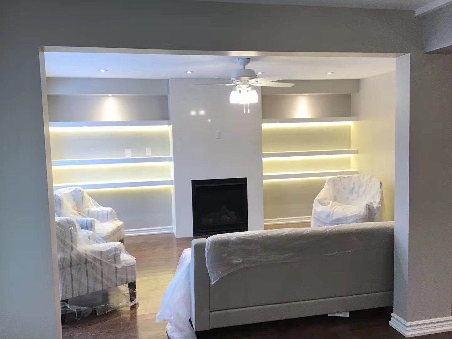 This Richmond Hill interior partial renovation highlights a modern living room upgrade featuring a custom fireplace feature wall with built-in illuminated shelving on both sides. Warm LED lighting enhances the display areas while creating a cozy and elegant ambiance. The renovated space includes upgraded flooring, recessed ceiling lights, and a clean contemporary layout designed for comfort and functionality. Completed by Reno Compass, this interior remodeling project adds both visual appeal and practical storage solutions, showcasing high-quality craftsmanship for homes across Richmond Hill and the Greater Toronto Area.