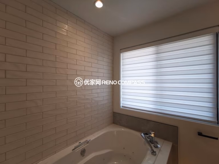 Bathtub area completed as part of a North York interior renovation, featuring a built-in soaking tub with a full-height tiled feature wall. Rectangular wall tiles create clean horizontal lines that visually extend the space, while the window introduces natural light and ventilation. Neutral tones and simple fixtures contribute to a calm, spa-inspired atmosphere designed for everyday comfort. This bathroom renovation was completed by a Toronto renovation company with a focus on material balance, layout efficiency, and long-term durability.
