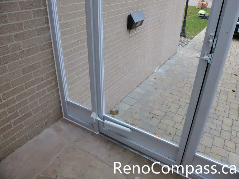Detail view of the storm door bottom seal and threshold connection in a North York storm door installation project. This image highlights the tight door fit, reinforced lower frame, and clean transition between the glass enclosure and stone flooring. Proper sealing helps prevent drafts, water infiltration, and heat loss while ensuring smooth daily operation and long-term durability of the entry system.