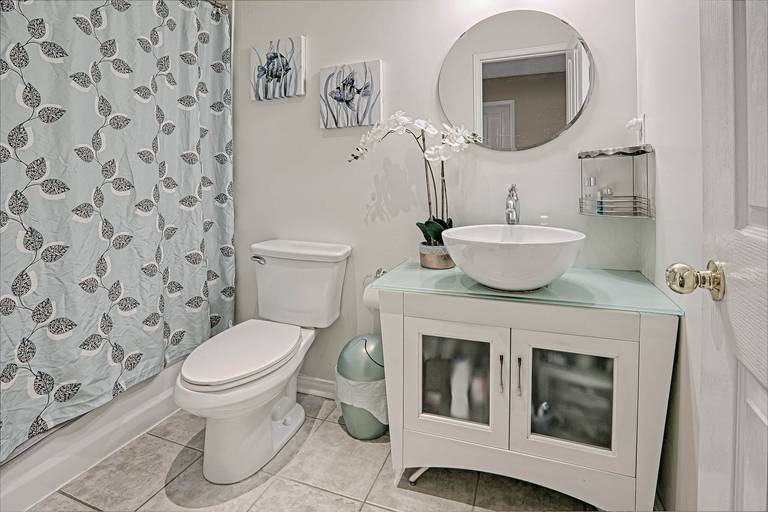 This warm and minimalist bathroom interior showcases a clean and cozy home design with modern fixtures, soft neutral tones, and functional storage solutions. Featuring a round mirror vanity, vessel sink, elegant cabinetry, and subtle decorative accents, the space reflects a comfortable and welcoming lifestyle. Perfect inspiration for homeowners seeking warm minimalist interior design and practical home styling ideas in Toronto and the GTA.