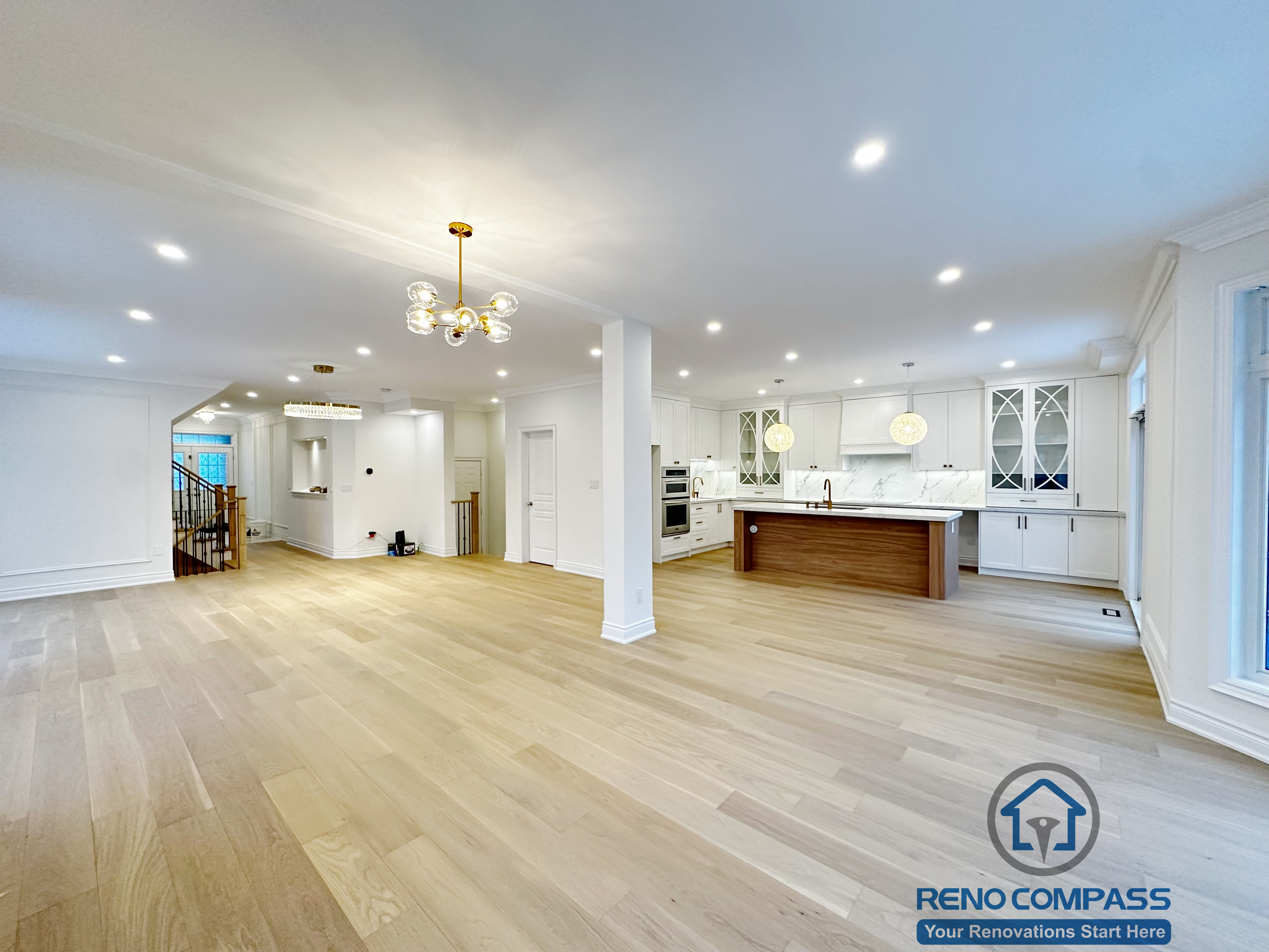 Full open-concept interior completed as part of a Vaughan interior renovation, showcasing seamless integration of living, dining, and kitchen areas. The space features wide-plank hardwood flooring, recessed ceiling lighting, custom columns, modern chandeliers, and a custom white kitchen with island. This cohesive layout highlights the craftsmanship of a professional Toronto renovation company.