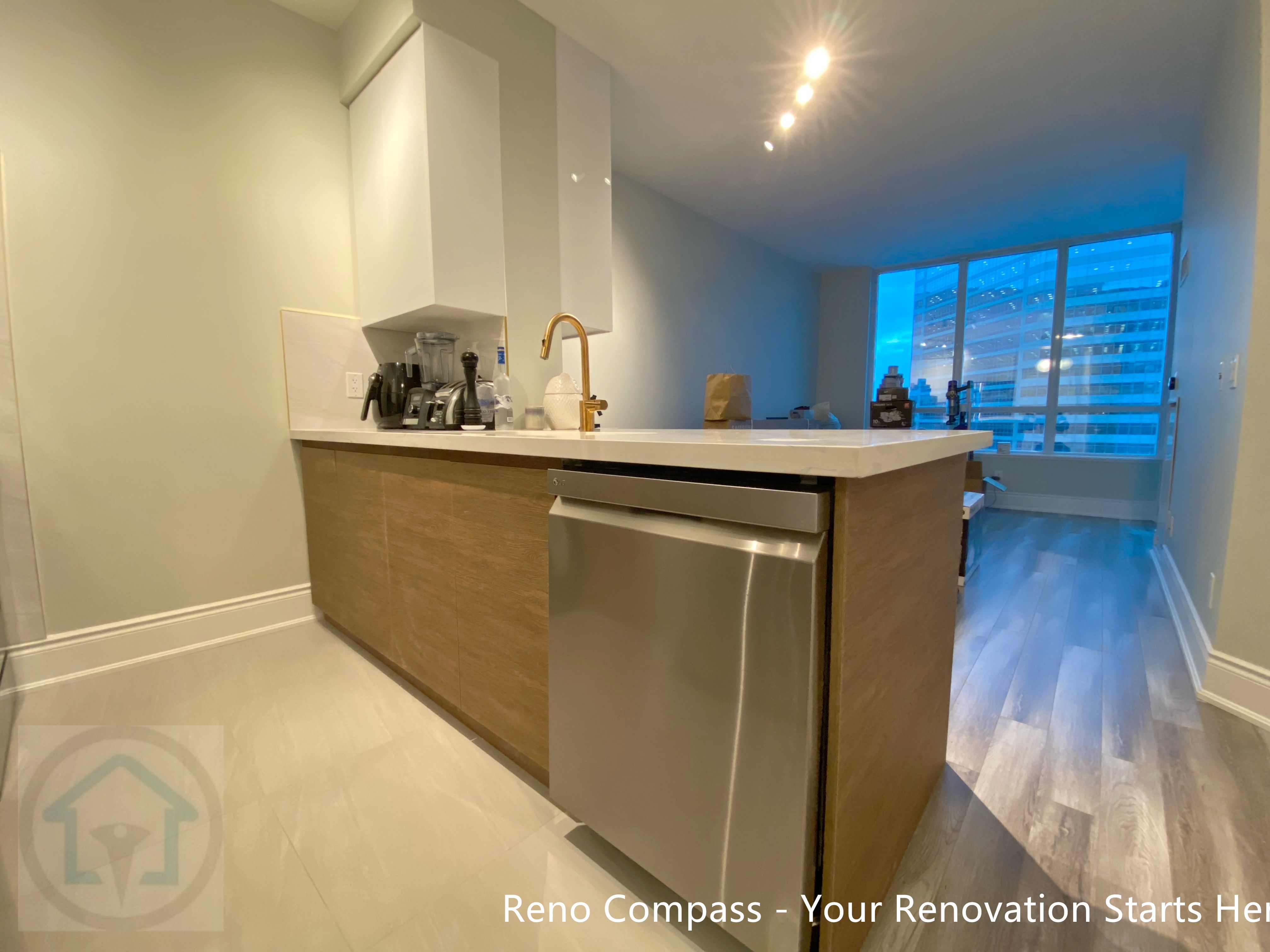 This image showcases a custom kitchen island designed for a North York condo renovation, featuring warm wood-tone cabinetry, an integrated dishwasher, and a quartz countertop with a brass faucet. The island serves as a functional transition between the kitchen and living area, improving workflow while maintaining a clean, modern appearance. Thoughtful lighting and streamlined finishes enhance both daily usability and the overall openness of the condo interior.