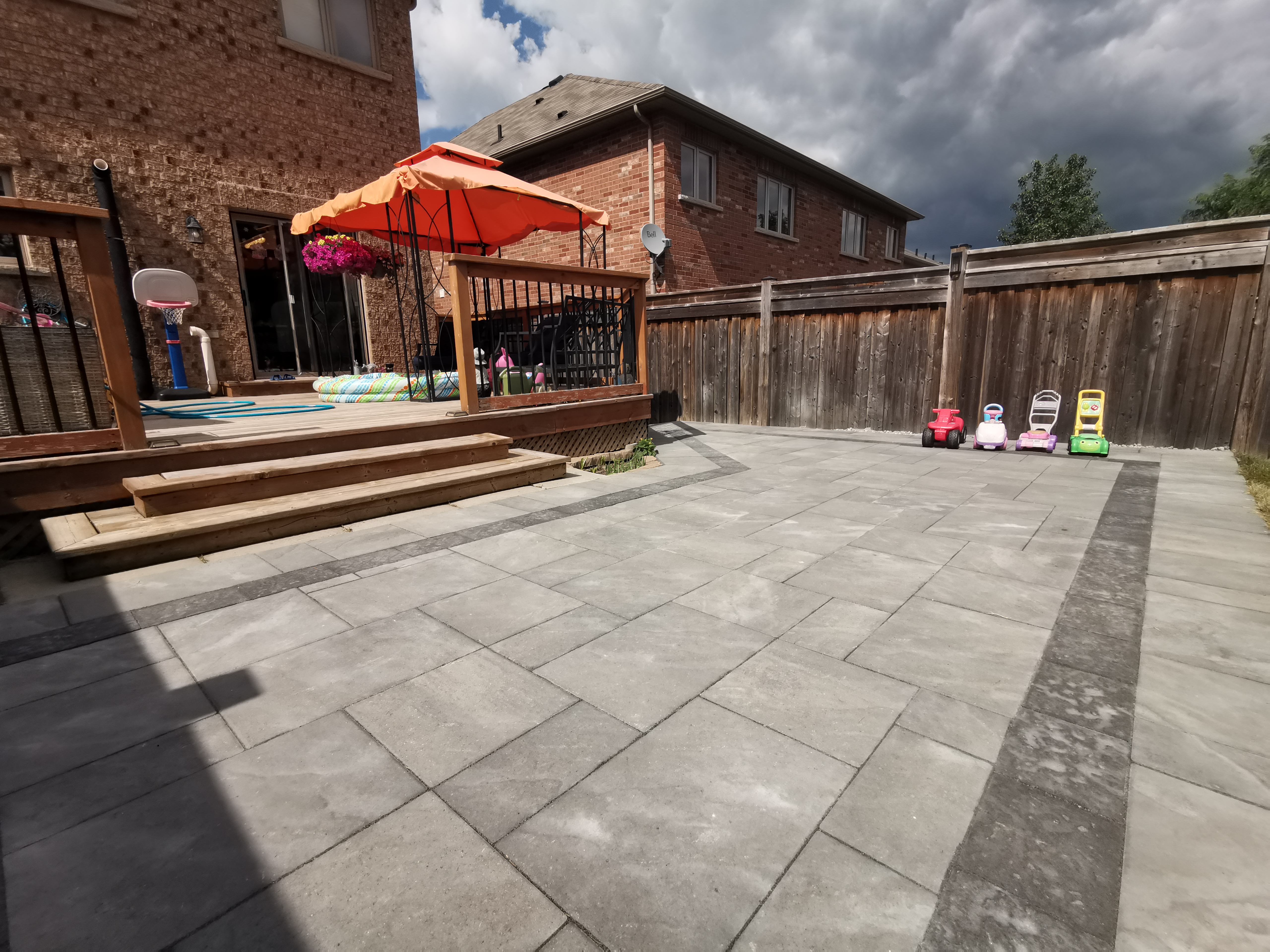 This Aurora backyard interlocking project features a spacious paver patio seamlessly connected to a raised wooden deck. Large-format concrete pavers provide a durable, level surface ideal for outdoor activities, family gatherings, and everyday use. The clean layout enhances drainage and long-term performance while maintaining a modern and low-maintenance finish. The interlocking patio creates a functional and inviting outdoor living space, perfectly suited for residential backyards in Aurora.