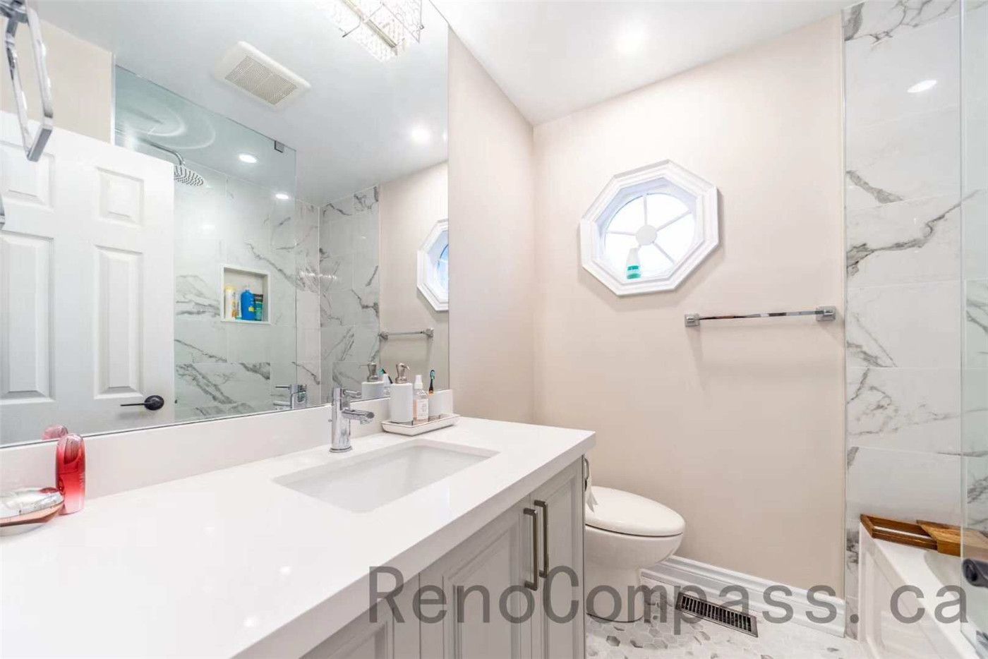 This modern bathroom is part of a North York interior renovation, featuring a clean and functional layout designed for daily comfort. The space includes a custom vanity with quartz countertop, an undermount sink, and sleek hardware for a refined look. Large mirrors and recessed ceiling lights enhance brightness, while marble-style wall tiles and a glass shower enclosure add a contemporary finish. Thoughtful material selection and efficient space planning reflect the quality and attention to detail expected from professional Toronto interior renovation projects.
