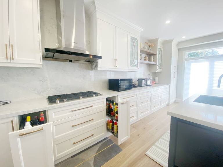 A detailed view of custom kitchen cabinetry completed as part of a Richmond Hill interior renovation. This kitchen renovation showcases full-height cabinets, integrated pull-out storage, quartz backsplash, stainless steel range hood, and efficient cooking-zone organization.