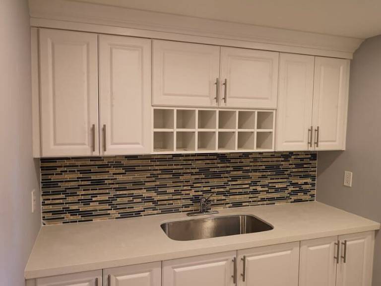 This Markham finished basement renovation features a modern kitchenette with custom white cabinetry, mosaic backsplash, and durable flooring in a bright open layout. Completed by a professional Toronto renovation company, the project creates a functional and stylish basement living space ideal for rental potential, entertainment, or extended family use.