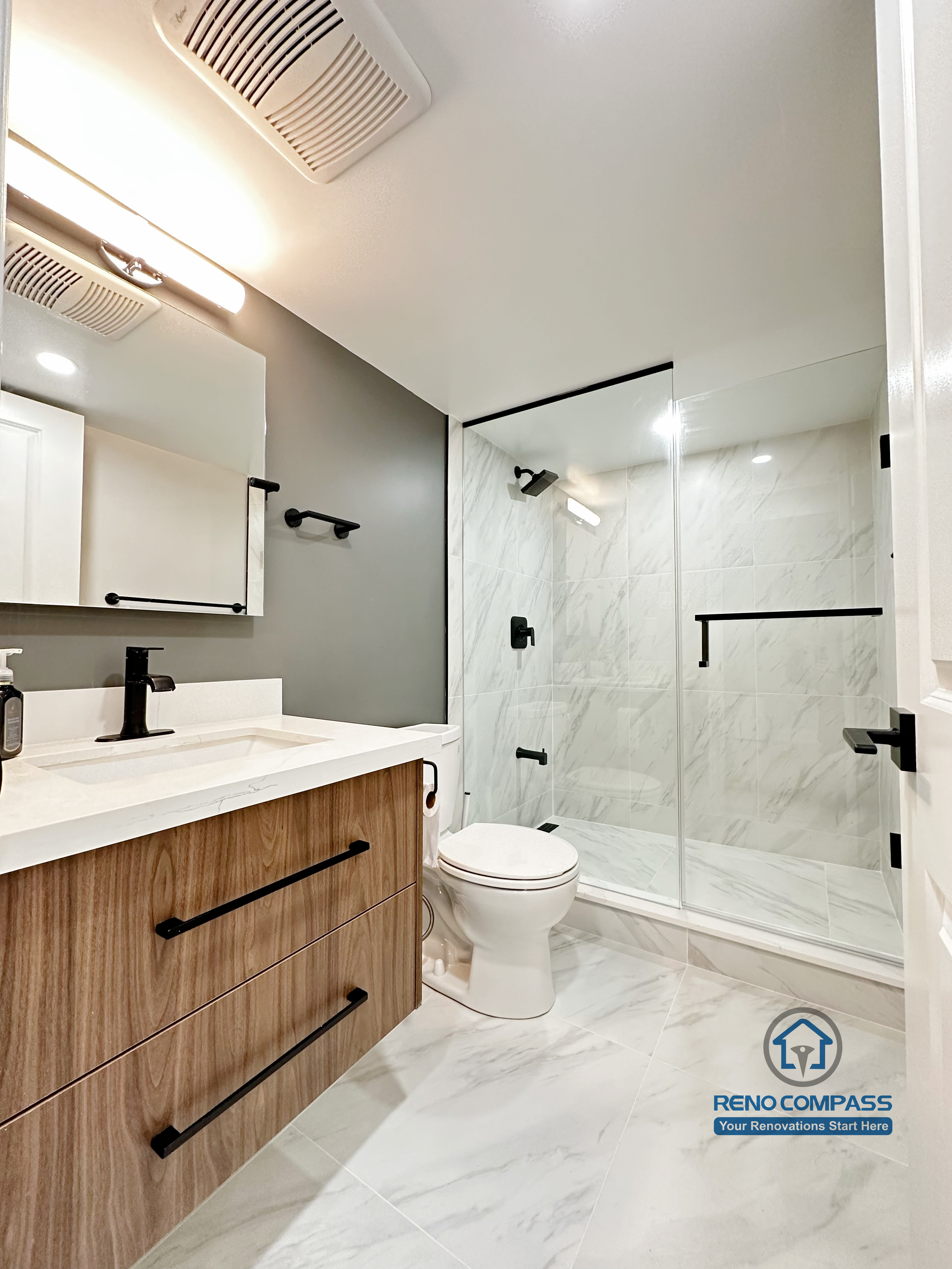 This Newmarket basement bathroom renovation features a modern wood-tone vanity, quartz countertop, and a sleek glass-enclosed shower with marble-look tile. The finished basement bathroom combines clean lines, black hardware accents, and efficient lighting, creating a bright and functional space designed for everyday comfort.
