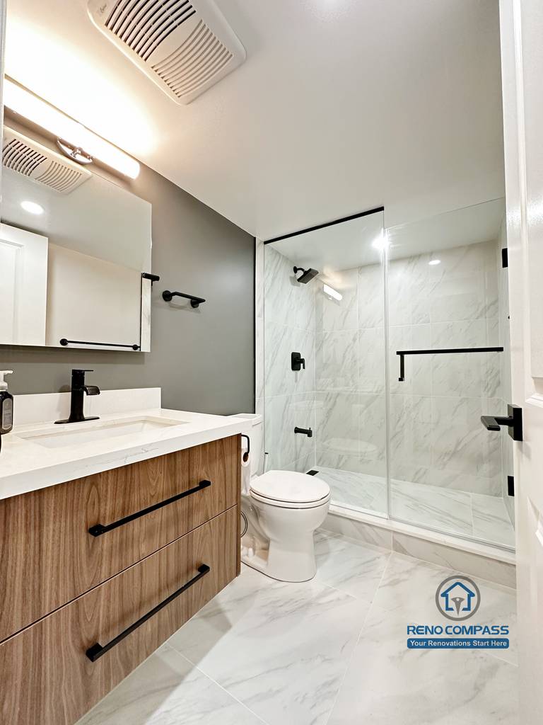This Newmarket basement bathroom renovation features a modern wood-tone vanity, quartz countertop, and a sleek glass-enclosed shower with marble-look tile. The finished basement bathroom combines clean lines, black hardware accents, and efficient lighting, creating a bright and functional space designed for everyday comfort.