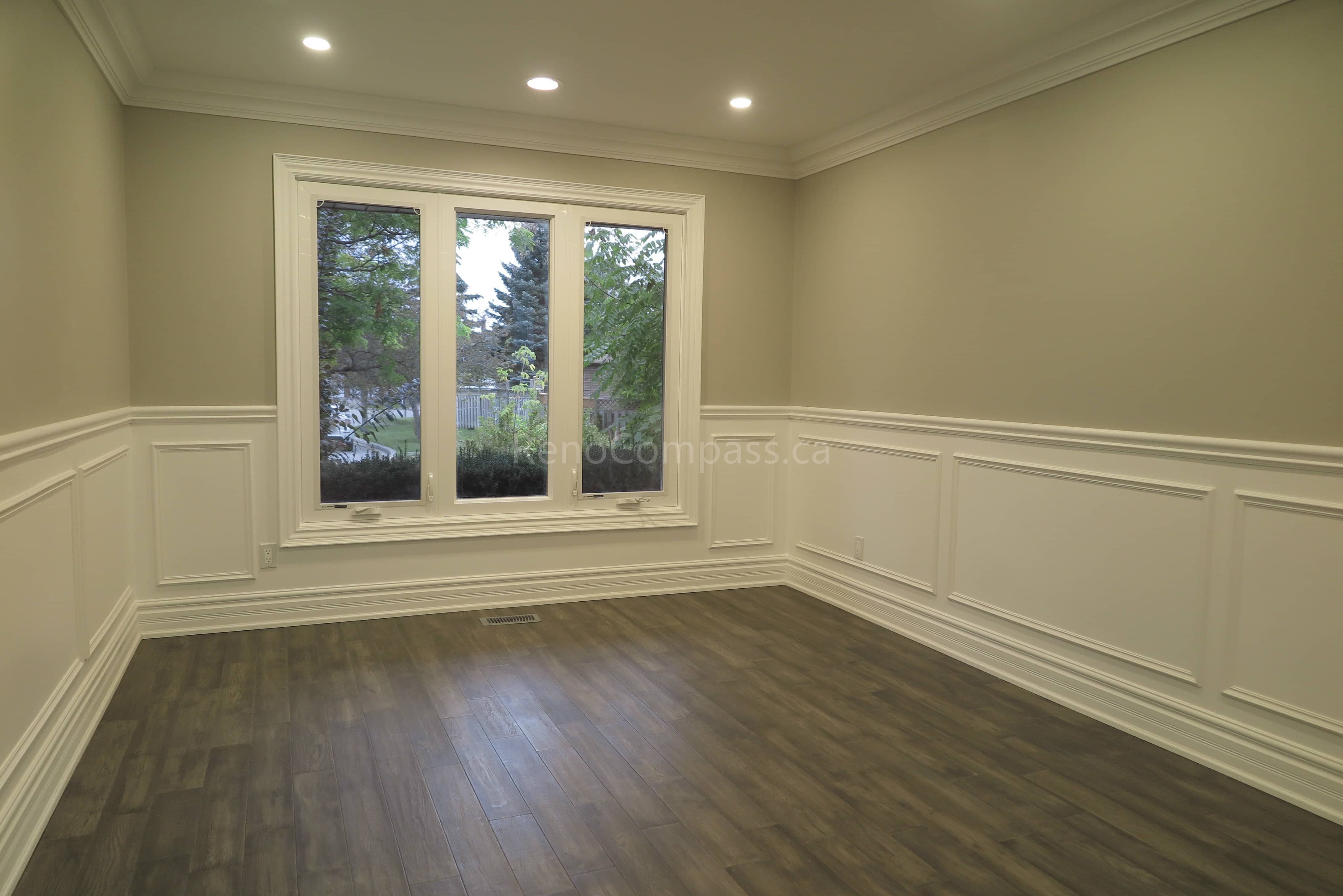 This Markham interior renovation showcases a bright and elegant living space featuring custom wall panel molding, crown molding details, and newly installed dark hardwood flooring. Recessed LED pot lights provide balanced lighting throughout the room, while large windows enhance natural light and openness. Completed by Reno Compass, a professional renovation contractor specializing in high-quality interior renovations and custom finishing services across Markham and the Greater Toronto Area.