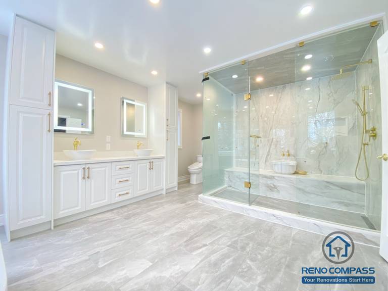 This Richmond Hill bathroom renovation showcases a bright and elegant design featuring a frameless glass shower enclosure, built-in bathtub, marble-style wall tiles, and gold-finish fixtures. The custom white vanity with integrated lighting mirror and large-format floor tiles enhance both functionality and visual openness. This project reflects high-quality craftsmanship and thoughtful layout planning for a modern bathroom renovation in Richmond Hill.