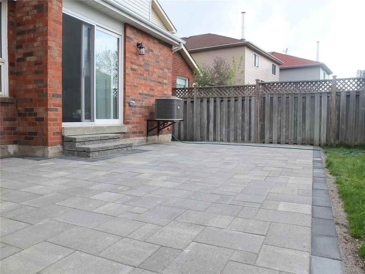 A completed backyard interlocking patio installation in Mississauga featuring large-format grey stone pavers, clean edge borders, and a modern low-maintenance outdoor design. This landscaping renovation improves outdoor usability and creates a durable patio space ideal for relaxation and gatherings. Completed by a professional Toronto Renovation Company, Reno Compass Inc., specializing in interlocking, landscaping, and exterior home upgrades across the GTA.