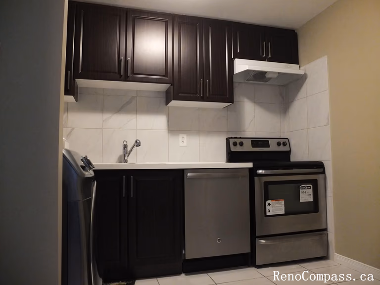 A sleek kitchen transformation in Mississauga featuring custom espresso-colored cabinetry, stainless steel appliances, and a clean white tile backsplash. Professional kitchen remodeling services by Reno Compass.