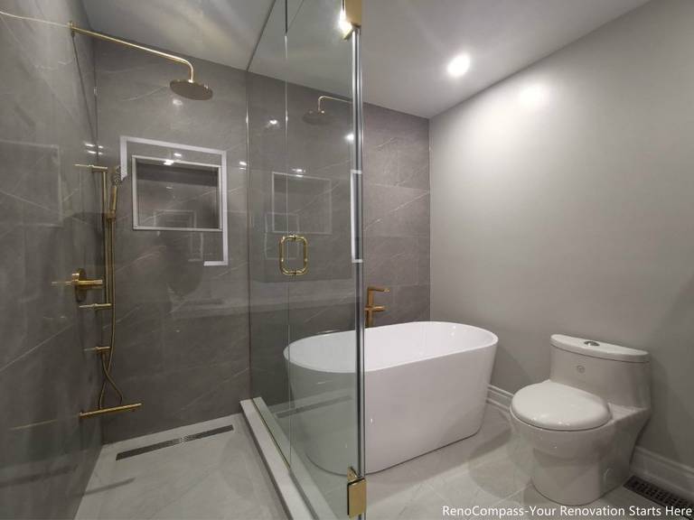 This Oakville master bathroom full renovation features a modern walk-in glass shower, freestanding bathtub, and sleek contemporary layout designed for comfort and luxury. Large-format marble-style tiles, premium gold fixtures, recessed shower niche, and linear drain create a clean, spa-inspired atmosphere. The combination of frameless glass enclosure, modern toilet installation, and bright lighting enhances both functionality and visual space. Completed by a trusted Toronto renovation company, this bathroom upgrade delivers long-lasting quality, elegant design, and increased property value for the homeowner.
