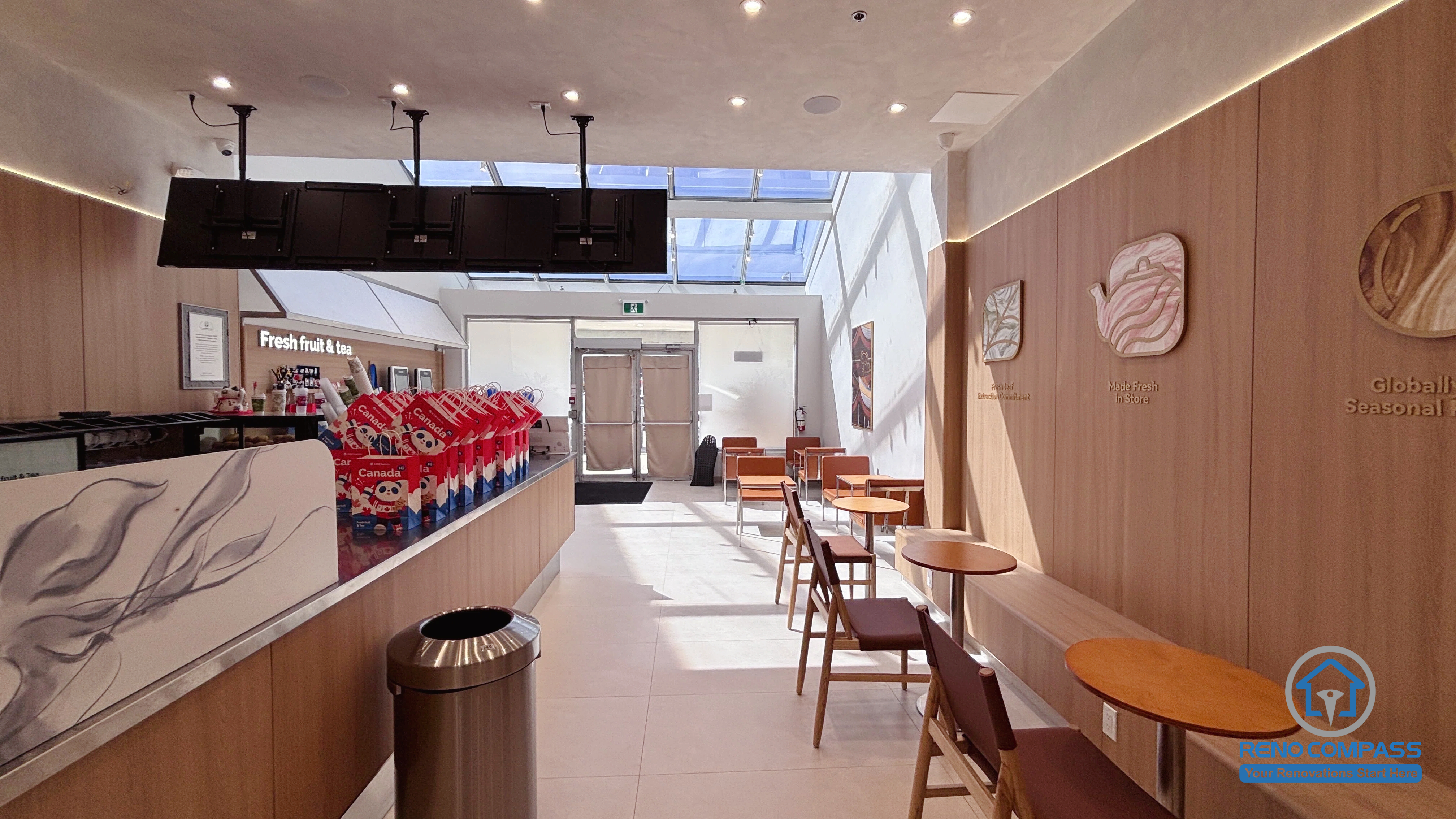 Completed TEABYDO bubble tea shop renovation in Richmond Hill featuring a modern café seating area, custom beverage service counter, warm wood-tone feature walls, skylight ceiling, integrated LED lighting, and clean minimalist commercial interior design. This bright and customer-friendly commercial renovation project was completed by Reno Compass serving Richmond Hill, Toronto, and the GTA.