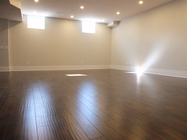 This Richmond Hill basement renovation features a bright and spacious open area designed for flexible living and entertainment. The space is finished with premium dark hardwood flooring, modern recessed pot lights, and neutral wall tones that enhance natural light from basement windows. A clean and open layout creates a comfortable environment ideal for a recreation room, home gym, or additional family living space, professionally renovated to improve functionality and home value.