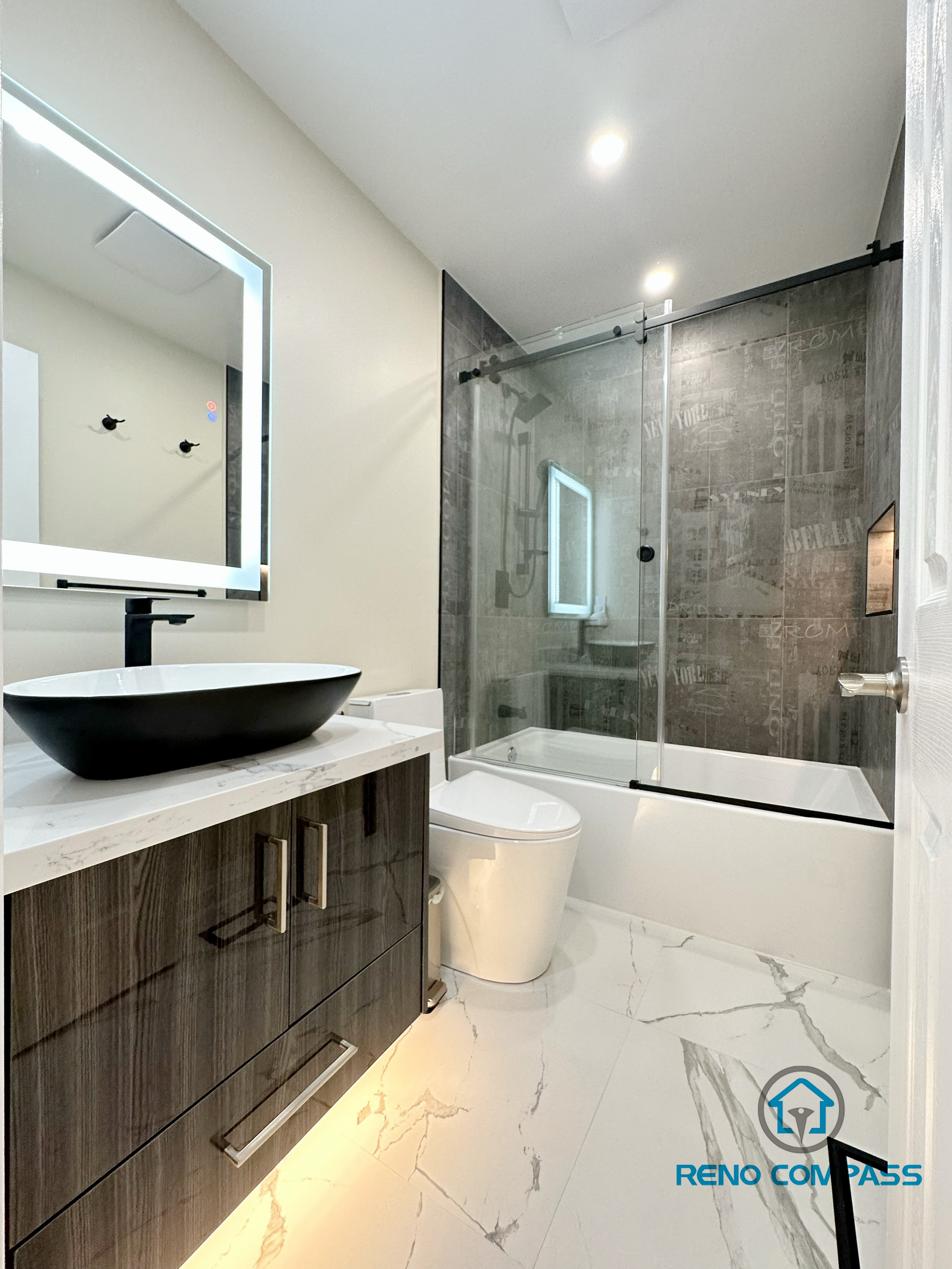 Full bathroom renovation in Vaughan featuring a modern floating vanity with integrated under-cabinet lighting, a backlit LED mirror, and a vessel sink on a quartz countertop. The space includes a frameless glass shower enclosure with large-format wall tiles, a sleek toilet installation, and marble-look porcelain floor tiles. This well-balanced layout reflects contemporary design and careful detailing, completed by a trusted Toronto renovation company with a focus on functionality, lighting, and clean finishes.