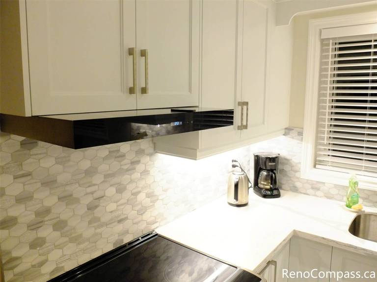 This North York home transformation features a bright open-concept kitchen flowing into the dining area. Key highlights include a custom waterfall quartz island with a built-in dishwasher, white shaker cabinets, and elegant large-format marble-look floor tiles. A perfect blend of modern style and everyday functionality.