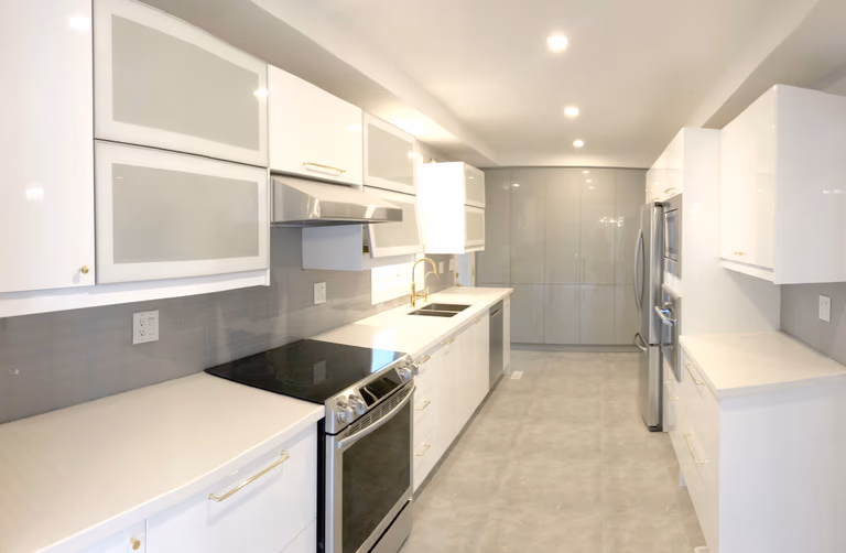 This Etobicoke kitchen renovation features a sleek modern layout with custom white cabinetry, quartz countertops, and stainless steel appliances for a clean and functional cooking space. The galley-style design maximizes efficiency, while under-cabinet lighting and recessed ceiling lights enhance brightness throughout the kitchen. A neutral backsplash and durable flooring complete the timeless look. Designed and completed by Reno Compass Inc., this kitchen upgrade focuses on practicality, storage optimization, and modern everyday living.