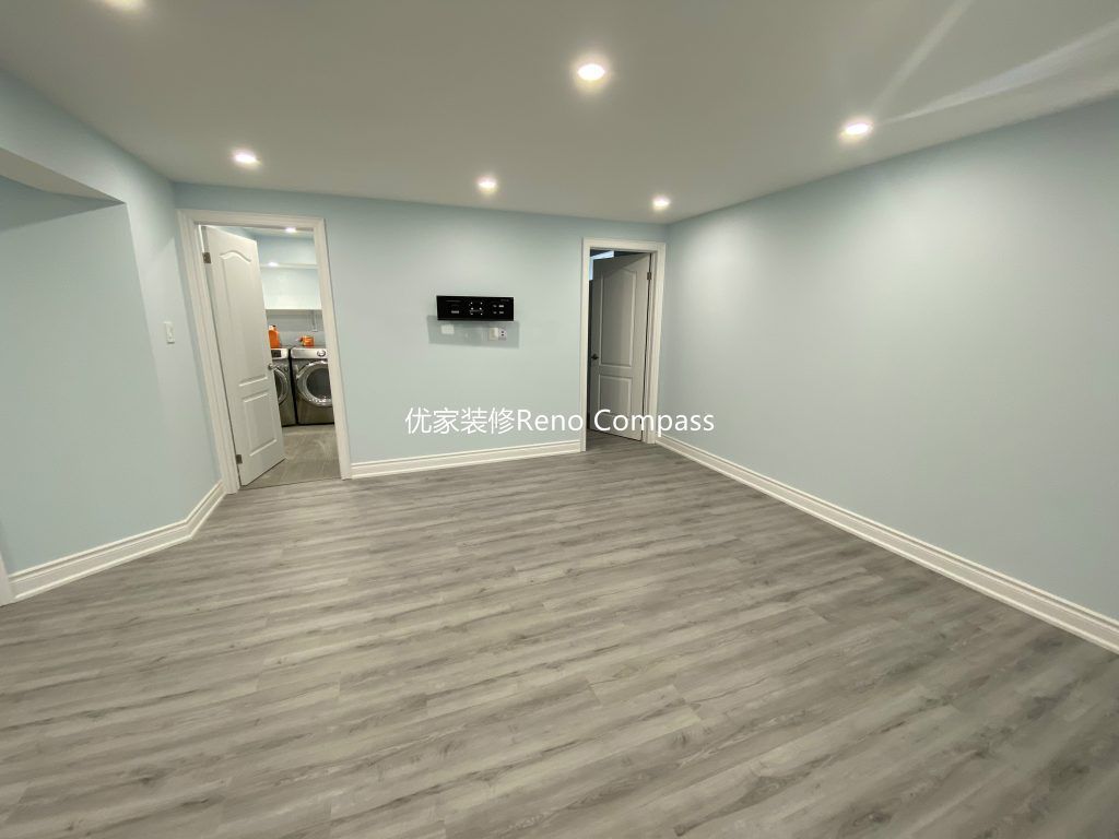 This Aurora basement renovation showcases a spacious open-concept living area completed by a professional Toronto renovation company. The upgraded basement features modern vinyl plank flooring, smooth finished ceilings with LED pot lights, and clean neutral wall tones that enhance brightness and comfort. The open layout seamlessly connects the living space to the laundry and bedroom areas, creating a functional and versatile basement ideal for family entertainment, rental use, or extended living. Contractor: Reno Compass Inc.